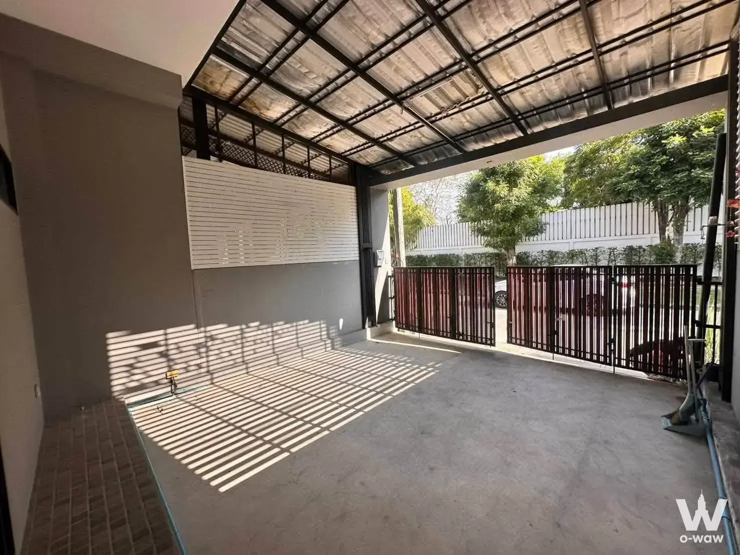 Covered carport for 3-bed house rental with corrugated metal roof, black steel trusses, and striped sunlight shadows