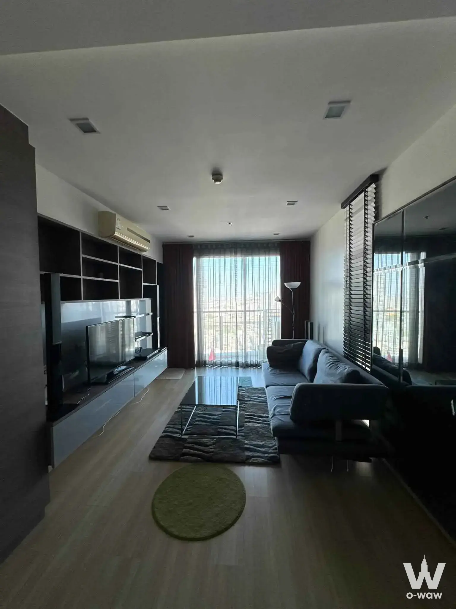 Furnished living room in Sky Walk Residences 1-bed condo with grey sofa, TV unit, and high-floor city views
