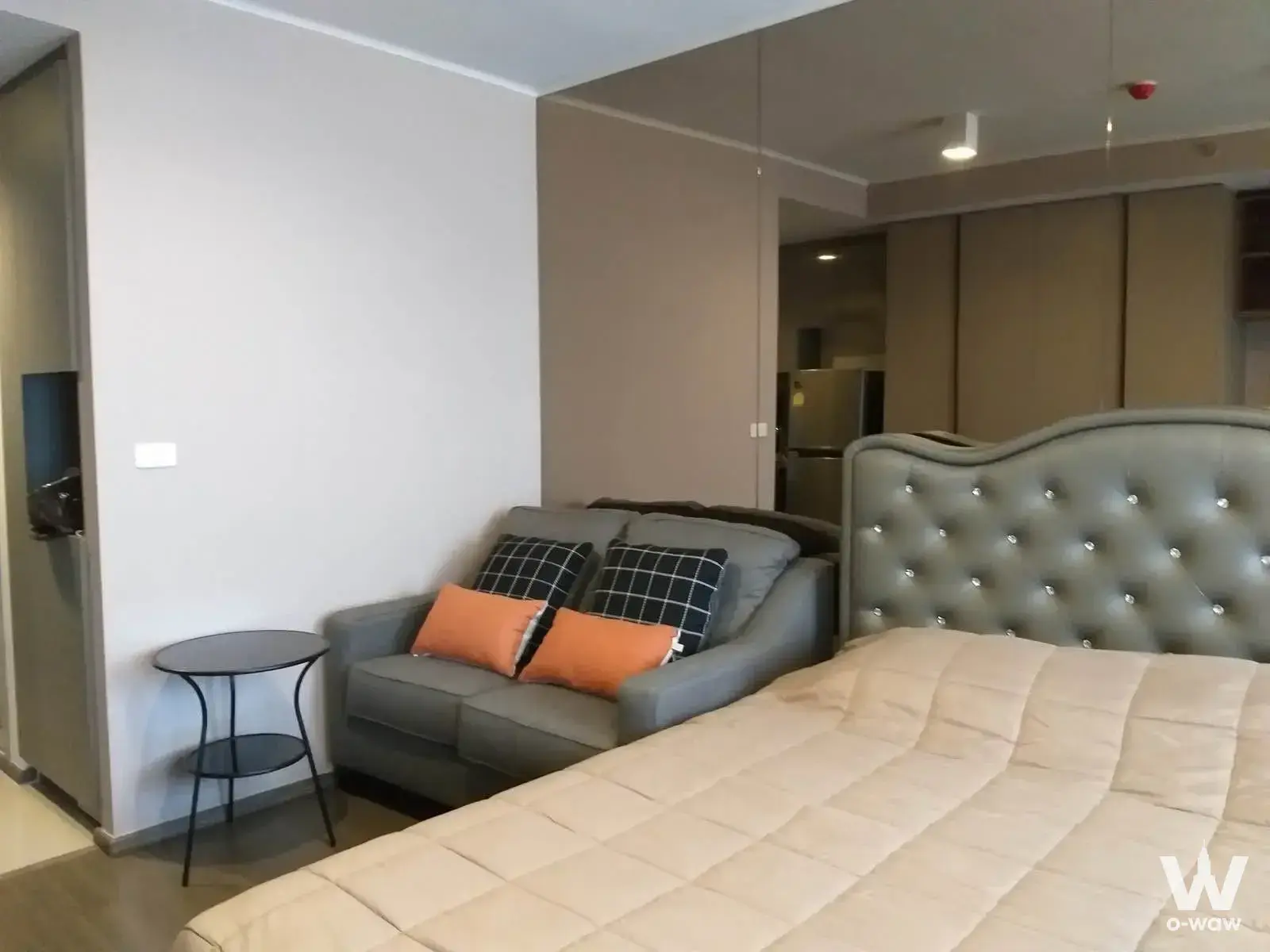 Ideo Sukhumvit 93 studio with grey sofa, orange pillows, and large wall mirror