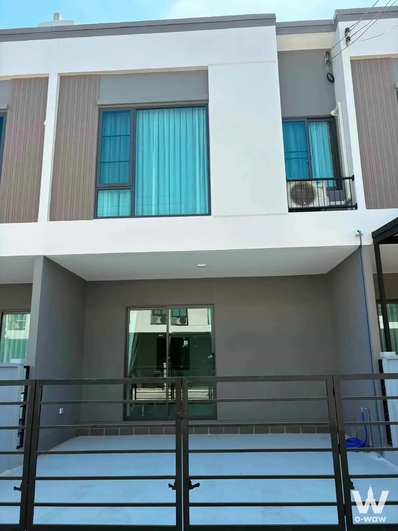Two-story exterior of a 3-bed house for rent in Pleno Sukhumvit-Bangna 2 with wood slats, large windows, and black gate