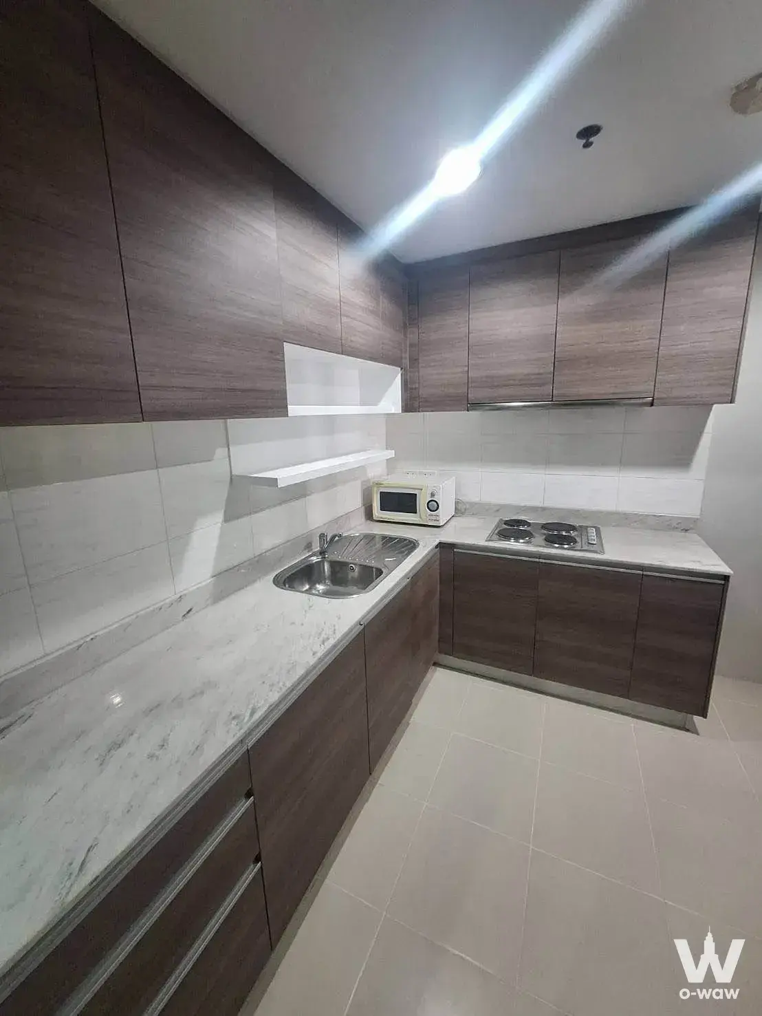 L-shaped kitchen in a Belle Grand Rama 9 condo with dark wood cabinets, quartz counters, and gas cooktop