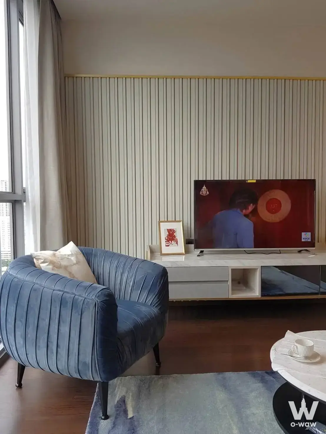 The living room in a 2-bed condo for sale at THE LINE Ratchathewi features a blue velvet chair and city skyline view