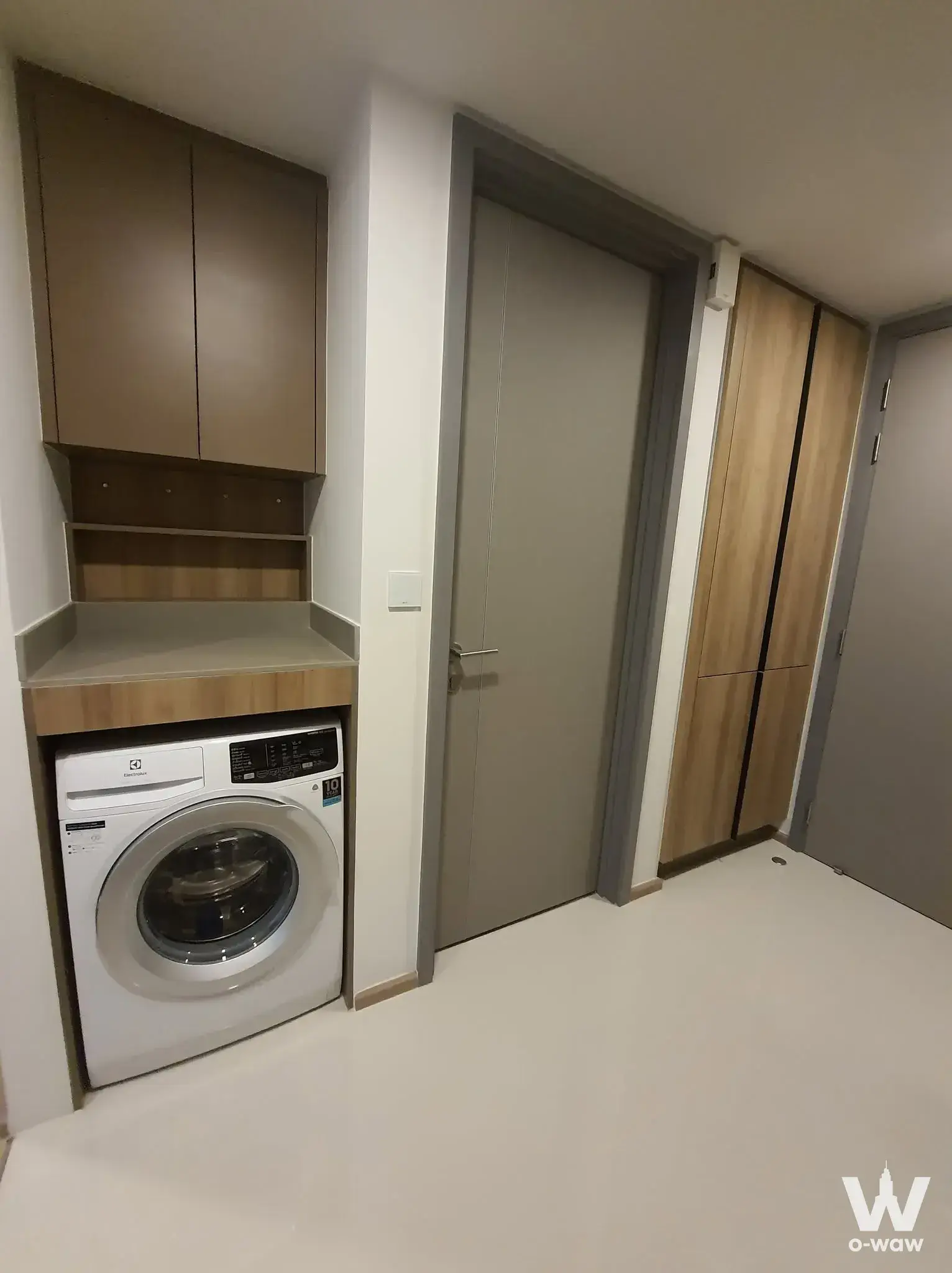 The utility corridor in a 1-bed condo for sale in TAKA HAUS has a built-in washer, taupe cabinets and grey doors