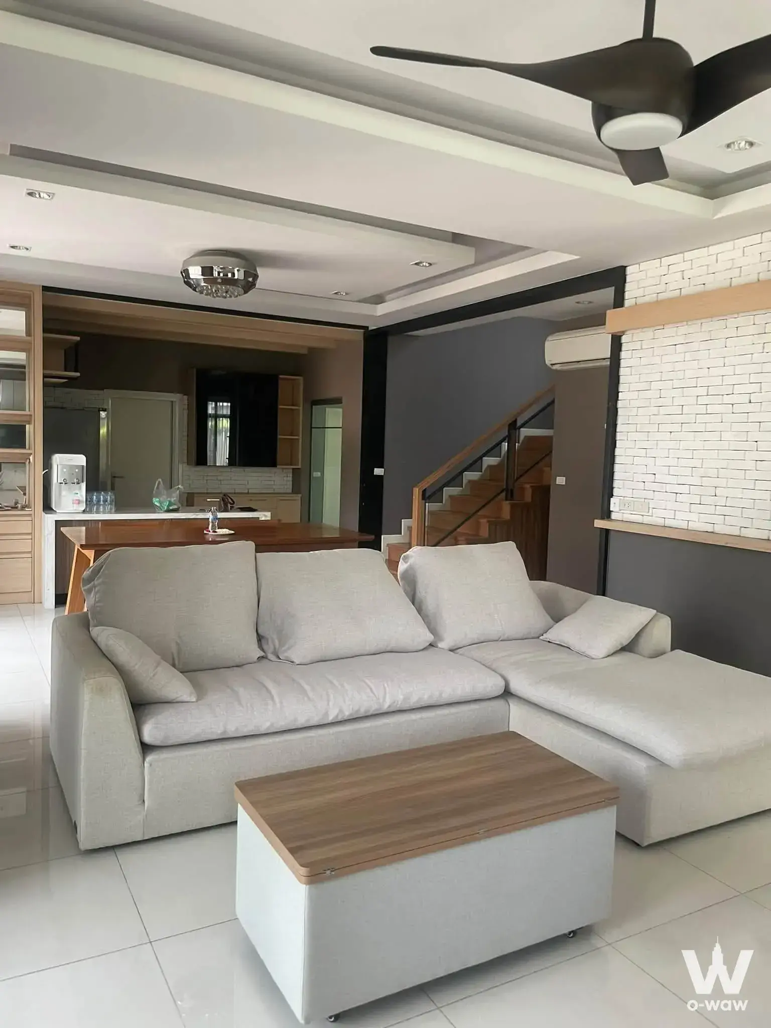 4-bed house for rent in The Palm Pattanakarn featuring grey sectional, wooden staircase, and open kitchen layout