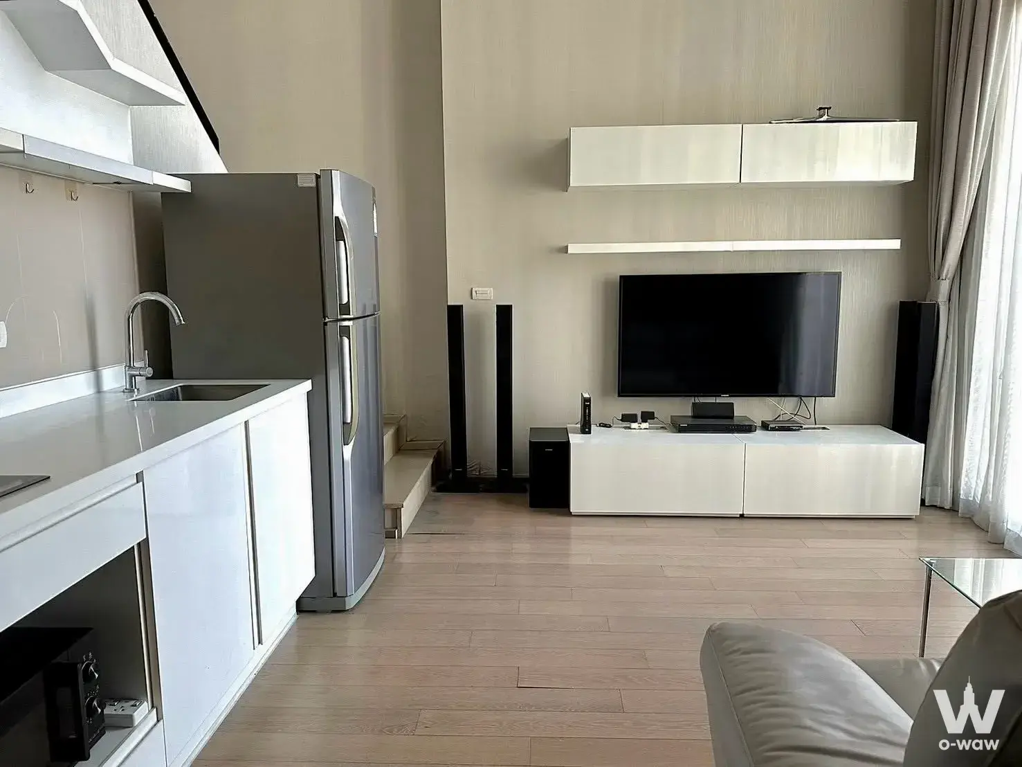 2-bed condo for sale in PYNE by Sansiri displaying an open-plan living area with a kitchenette, beige laminate floors, and a