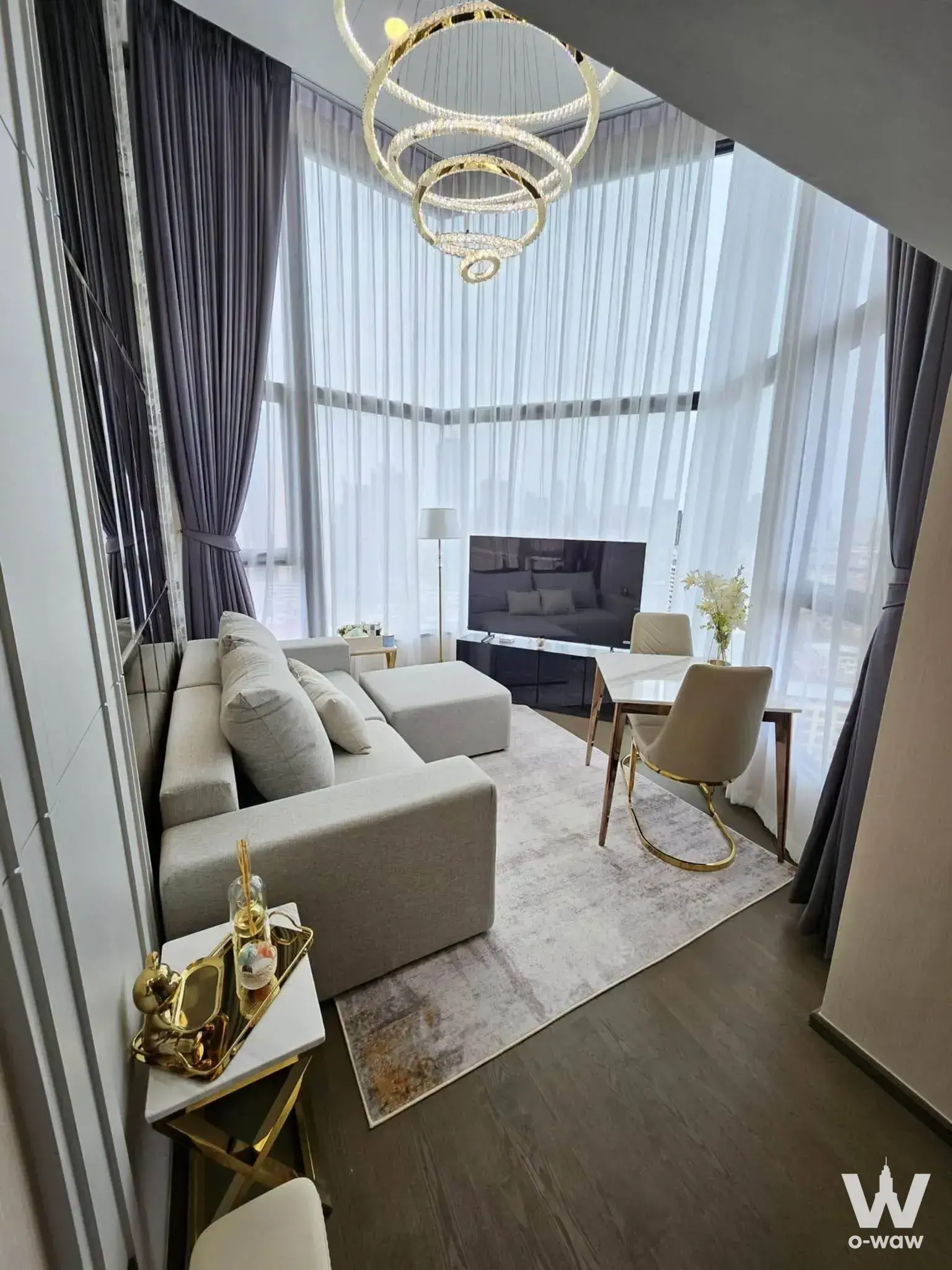 Living room in a 2-bed Park Origin Chula-Samyan condo with grey sectional, gold chandelier and city view