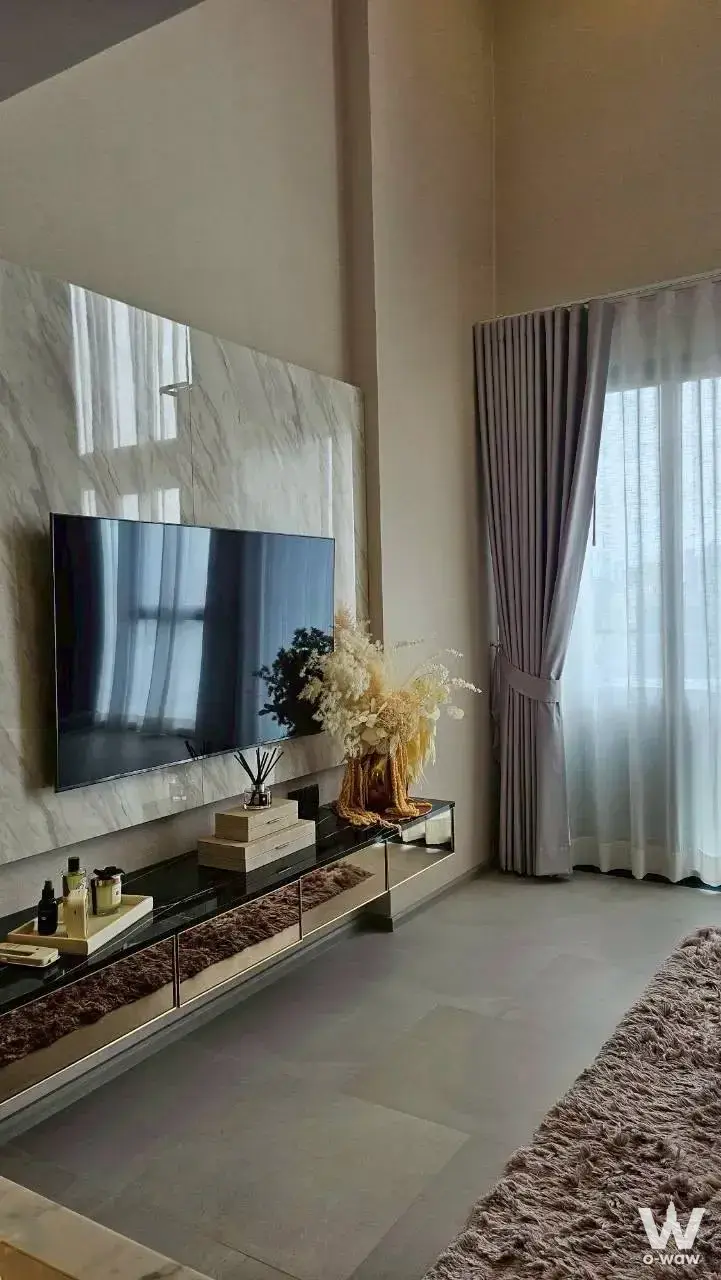 Bright bedroom in a Cooper Siam condo featuring a marble TV wall and floor-to-ceiling windows with grey drapes