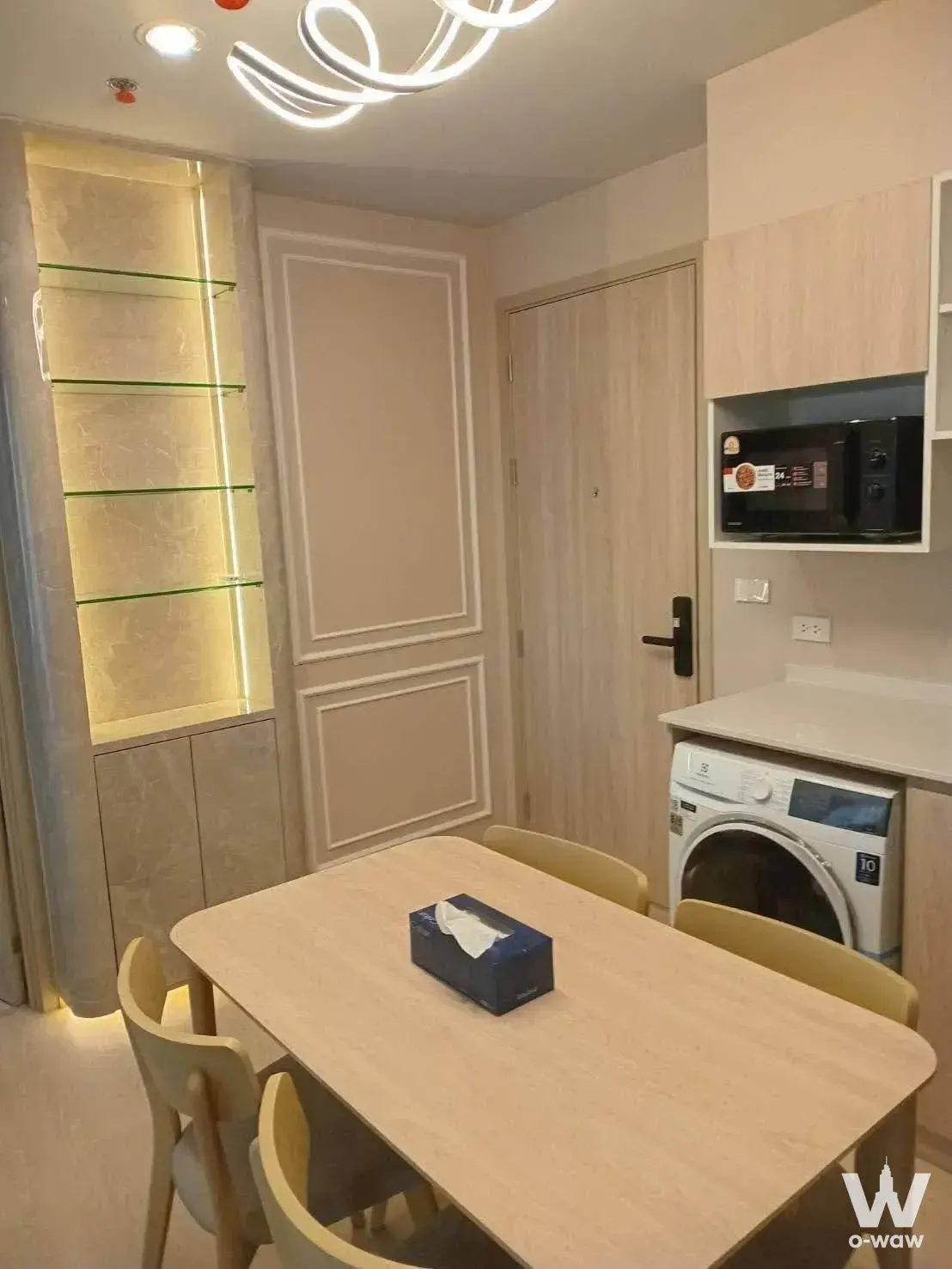 Dining area in Nue Mega Plus Bangna with light wood table and illuminated glass display niche