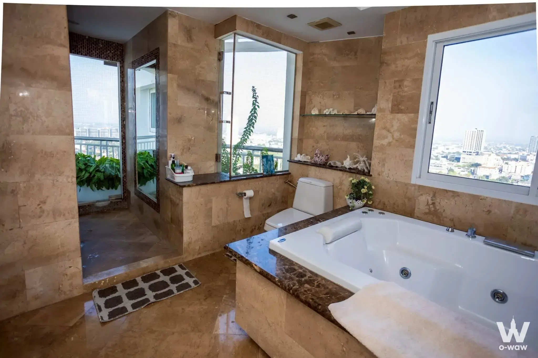 Luxury master bathroom with beige marble, jetted tub, and city skyline views at Saranchol Condominium