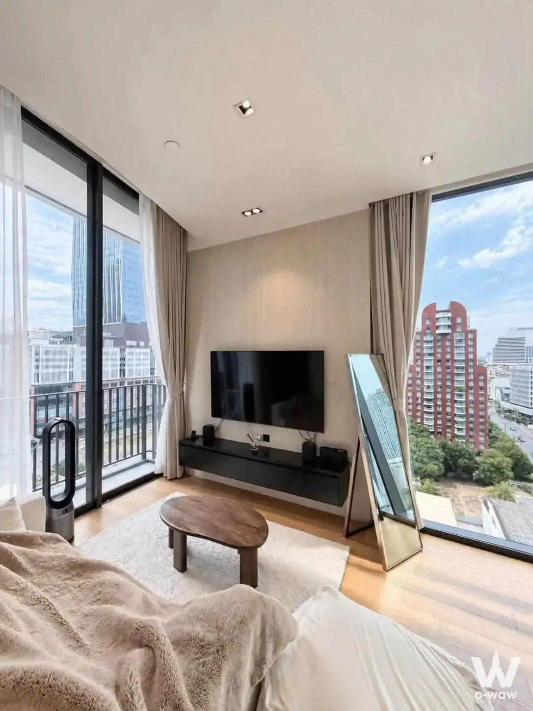 High-floor condo bedroom-living combo with city skyline view, walnut coffee table, and floor-to-ceiling windows at NOON