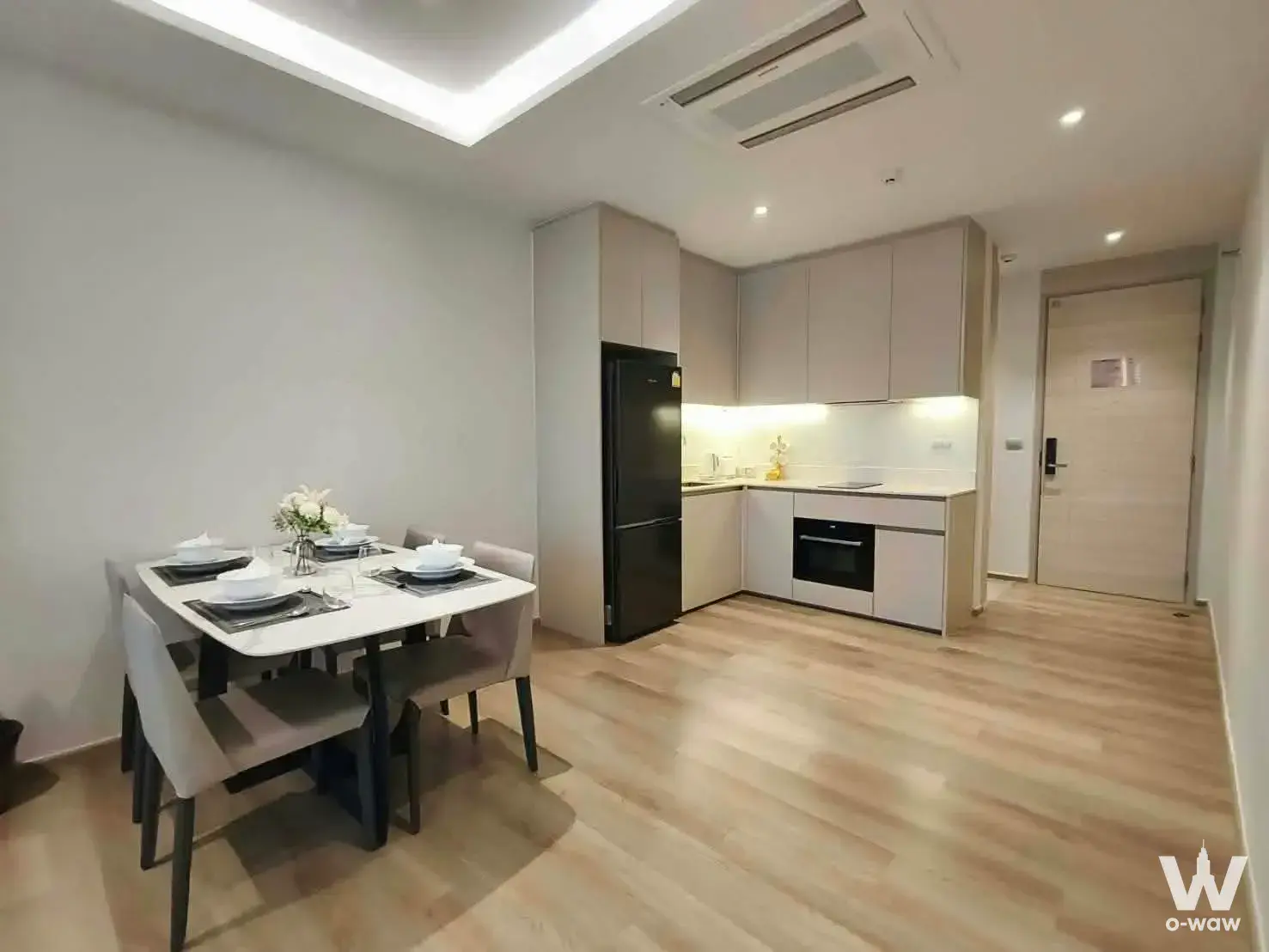 This 1-bed Bearing Residence condo shows an open-plan dining and kitchen with light wood flooring and matte beige cabinets