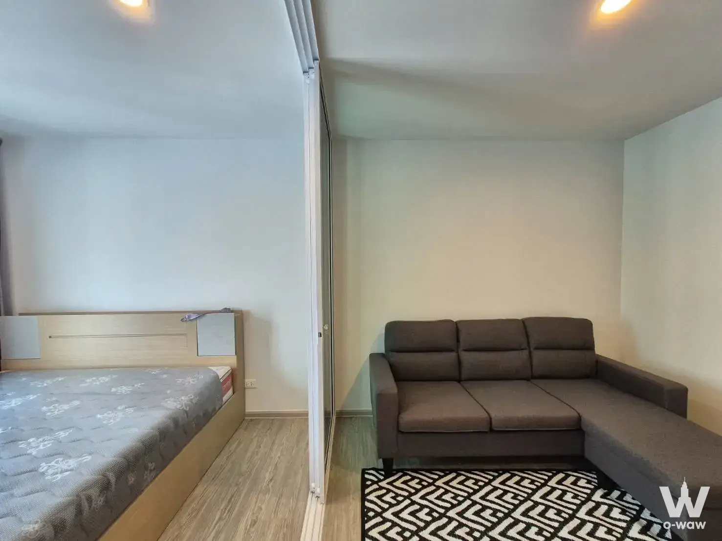 Compact living space in a Regent Home Bangna condo with L-shaped brown sofa and queen bed area