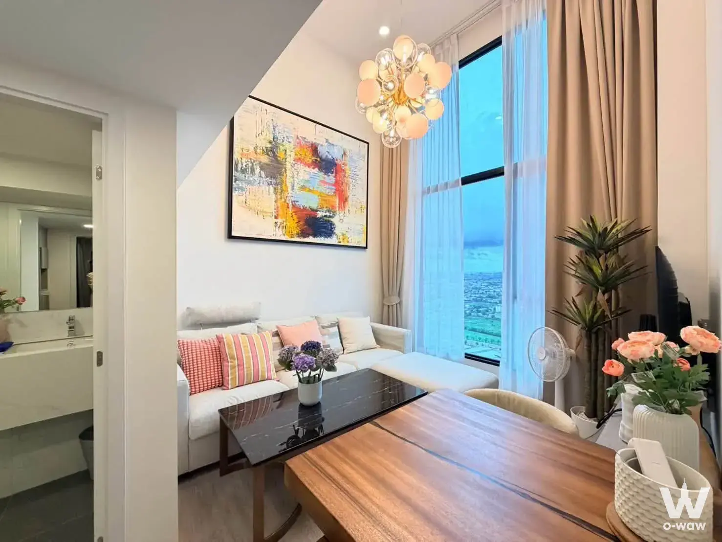 Living room with L-shaped sofa and city skyline view in Origin Plug Play Nonthaburi Station 2-bed condo for rent