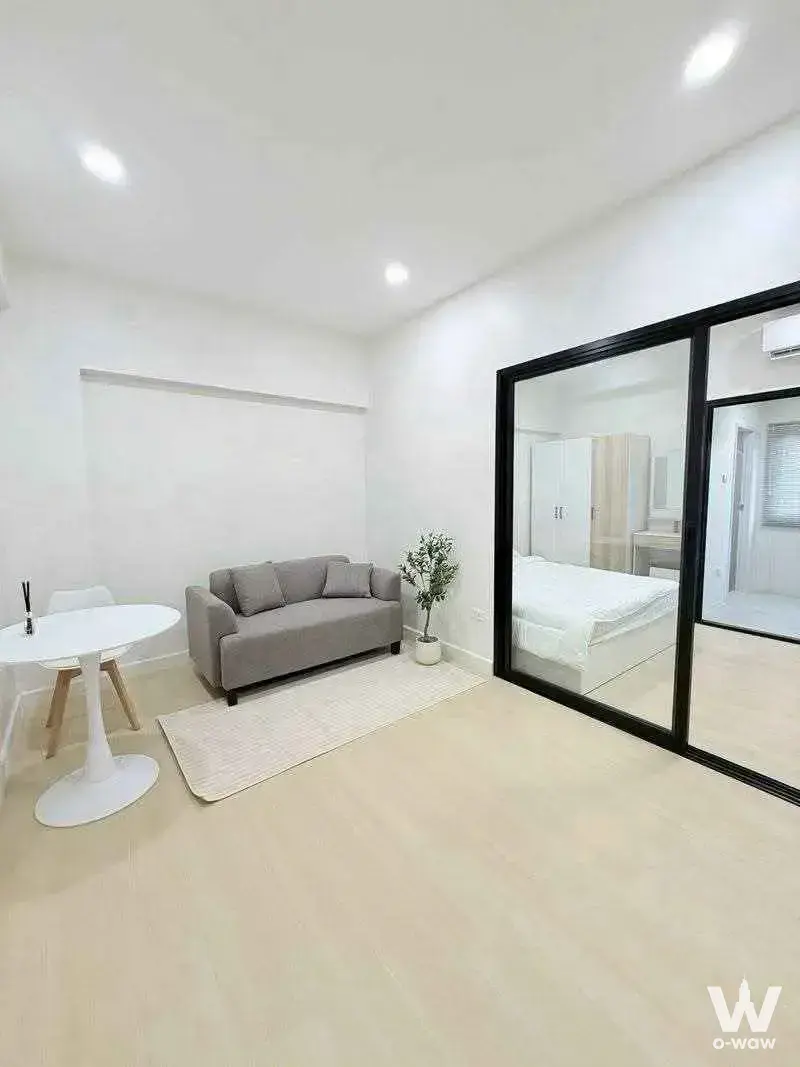 PP Condominium open-plan studio with grey sofa, glass partition, and minimalist white and wood decor