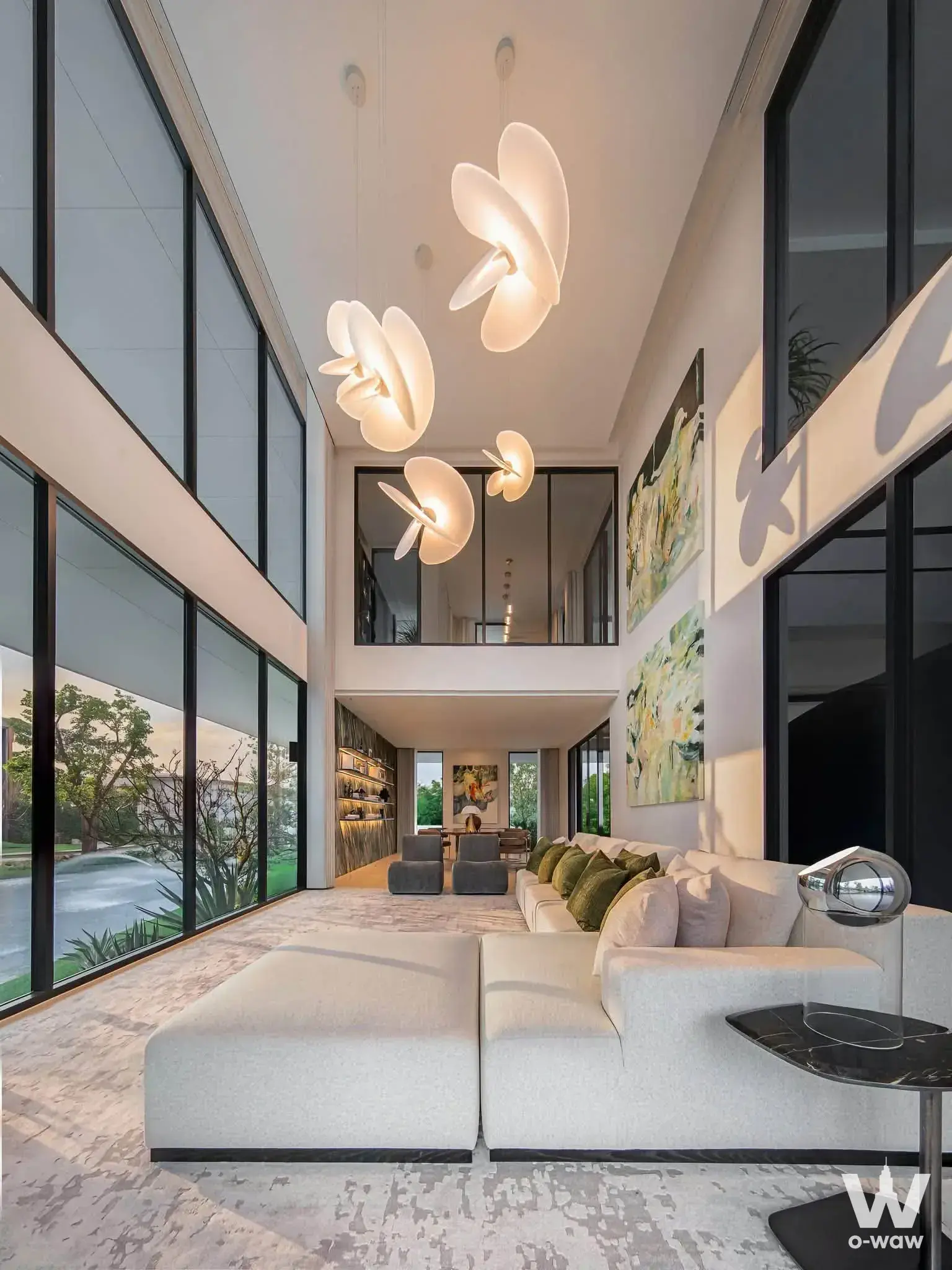 Double-height living room with white sectional sofa and pendant lights in a luxury 0-bed house for sale in Setthasiri Don