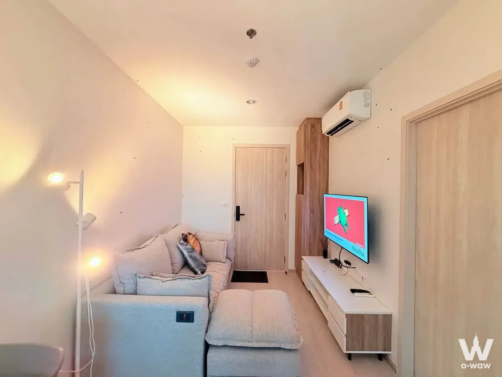 A 1-bed condo for rent at NUE Noble Faichai has a living room with a grey sofa, TV and wood-grain storage