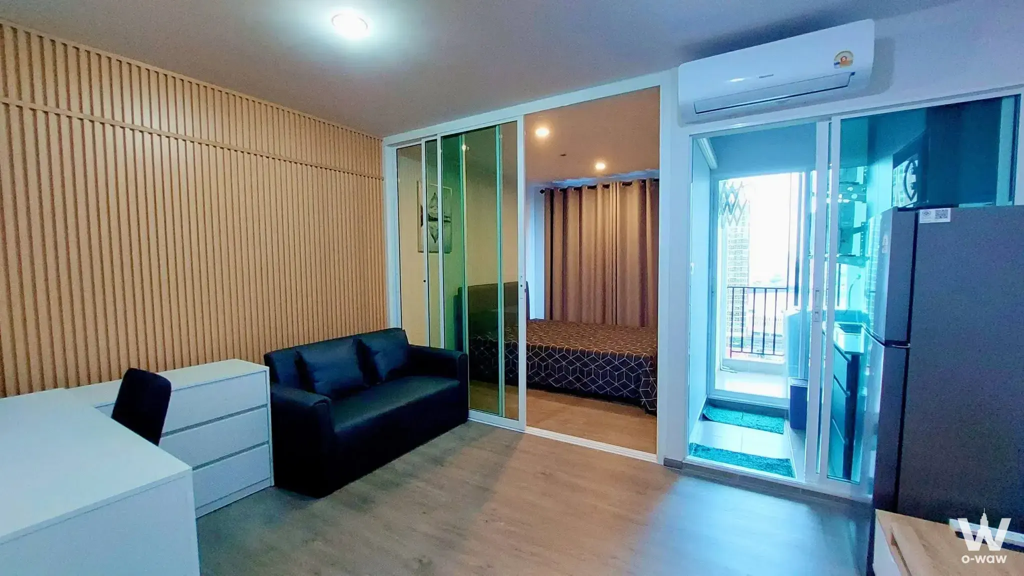 Open-plan condo in Regent Home Bangna featuring a glass partition, white desk, and compact kitchenette