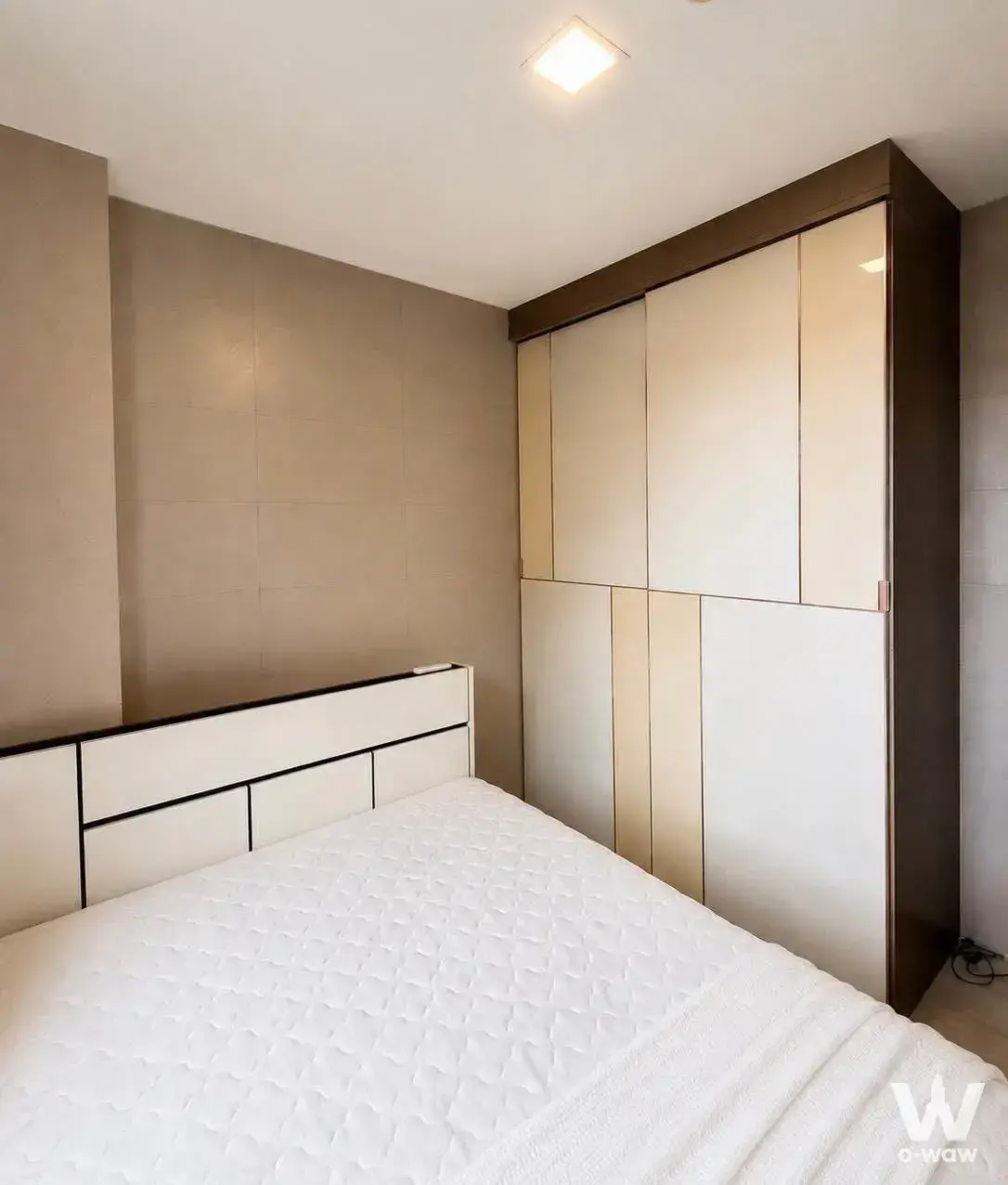 Bedroom in a 2-bed condo for sale at Maxxi Condo, featuring a queen bed with geometric headboard and dark wood wardrobe