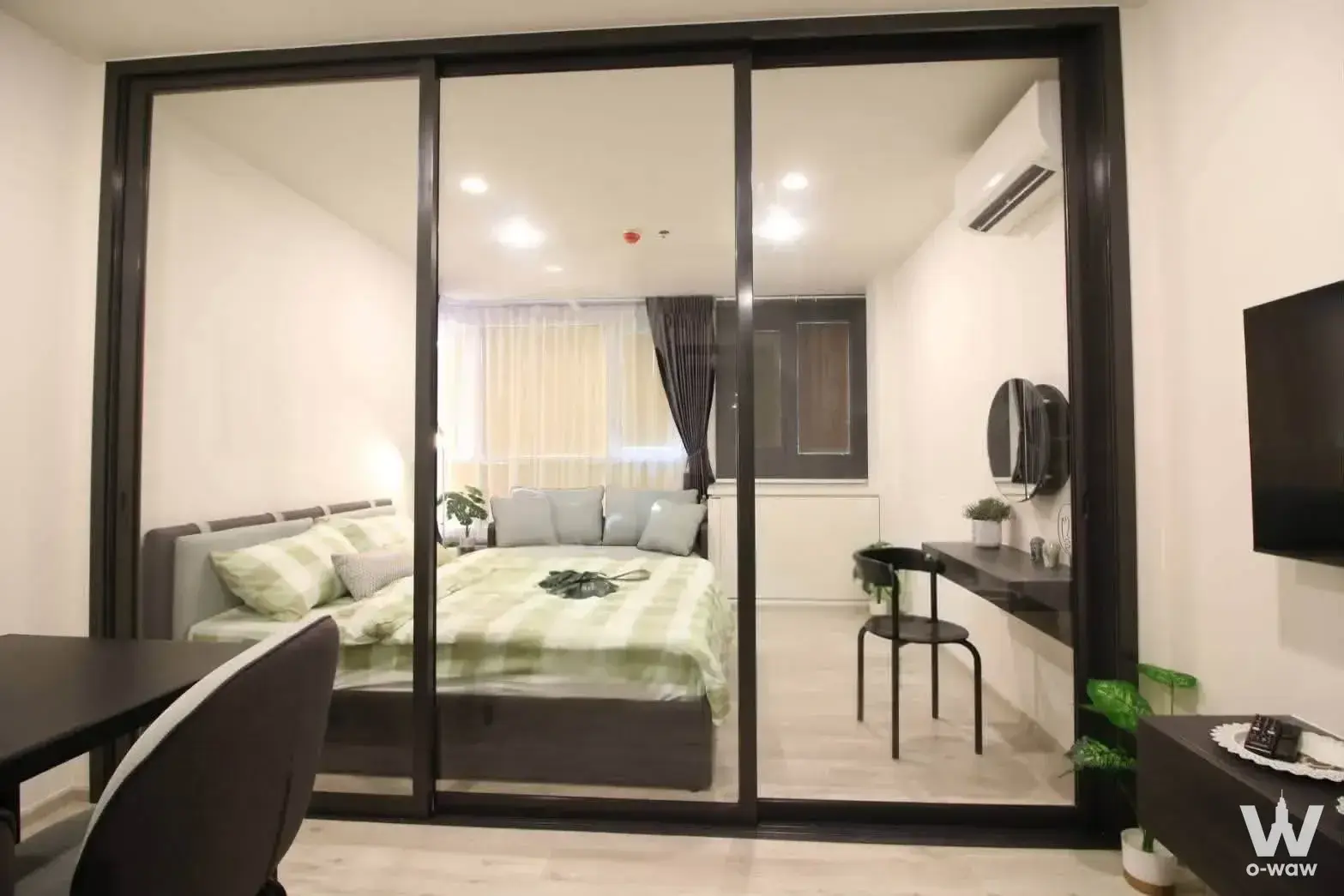 1-bed condo for sale in XT HUAIKHWANG studio with glass partition, green checkered bedding, and minimalist decor