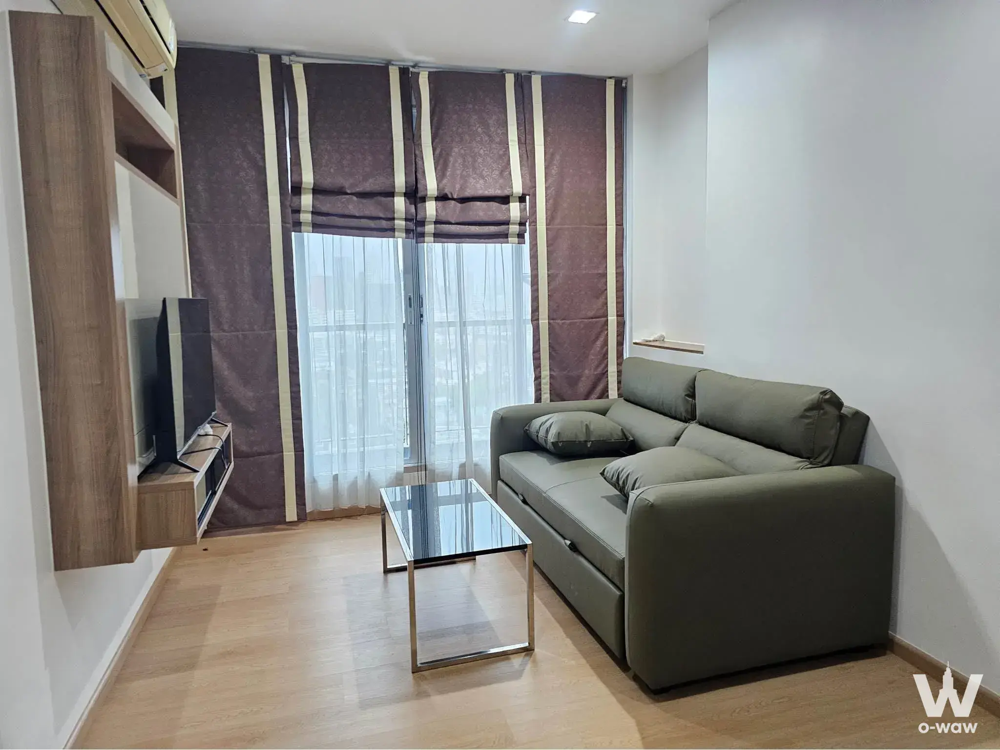 Living room in RHYTHM Phahon-Ari condo featuring olive sofa, oak floors, and city view