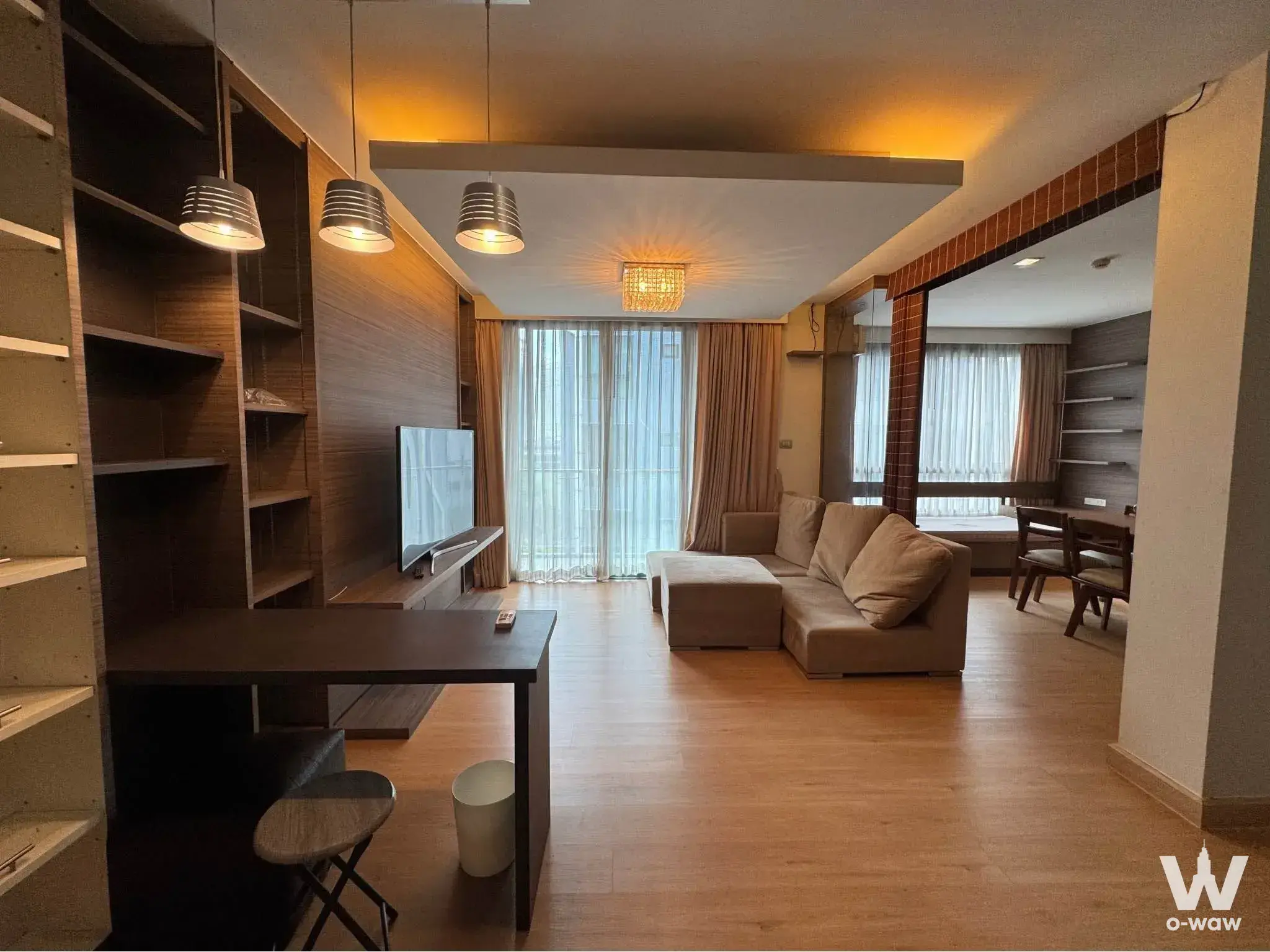 Dark wood feature wall with TV and beige sectional sofa in an Issara@42 1-bed condo living room