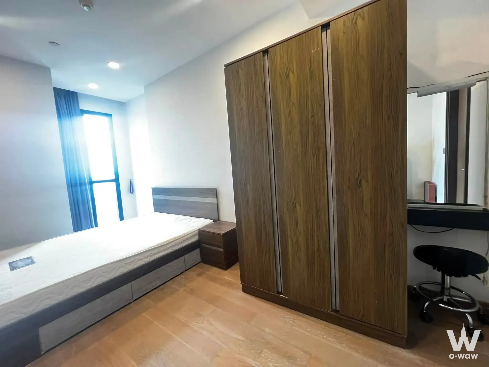 Bright bedroom in Ashton Chula-Silom condo featuring a grey bed with storage drawers and a large wooden wardrobe