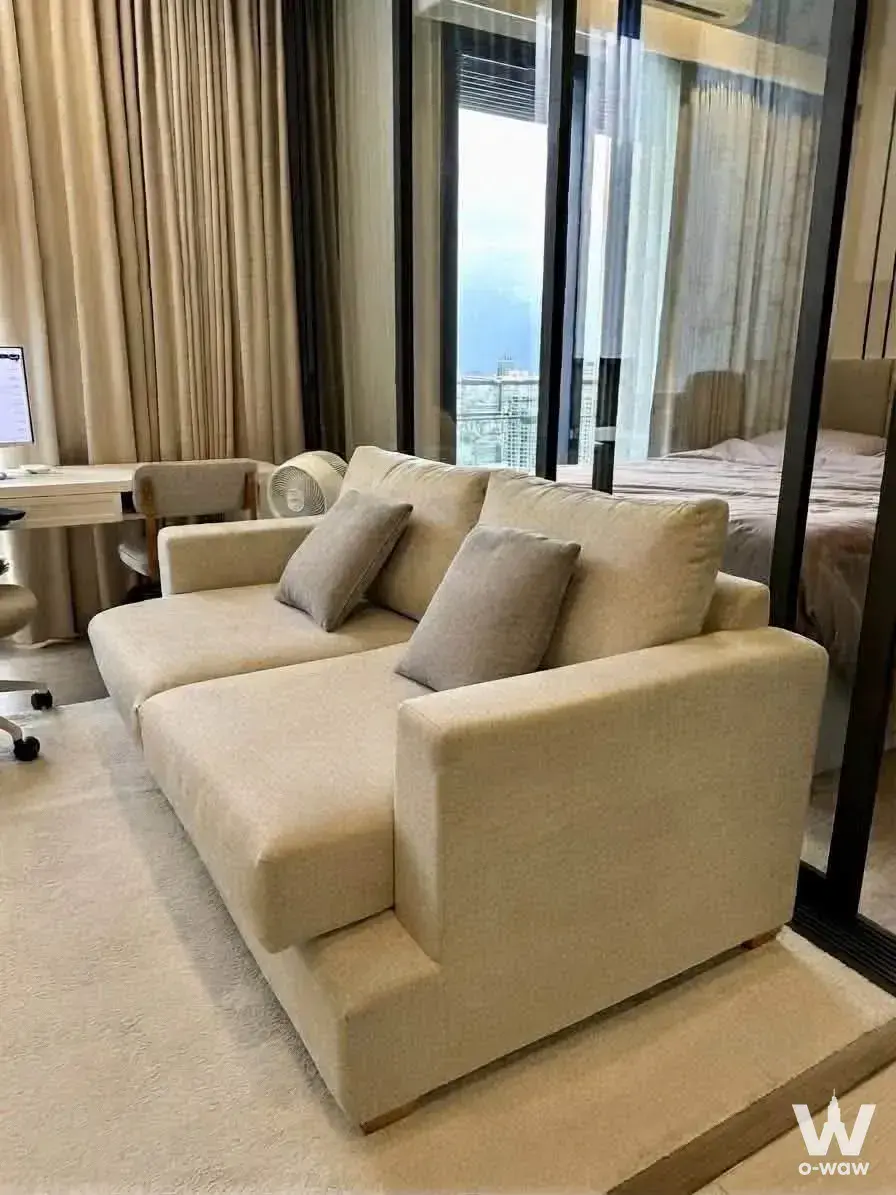 1-bed The Crest Park Residences studio with beige sofa, glass partition bedroom, and high-floor city skyline view