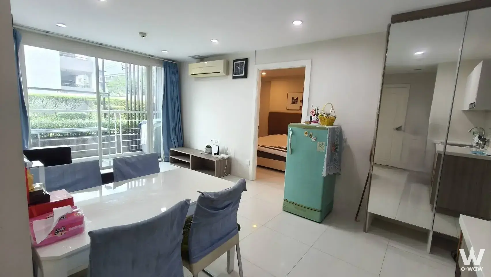 Open-plan living dining area in ELEMENTS SRINAGARINDRA CONDO, featuring white glossy floors, large dining table with blue