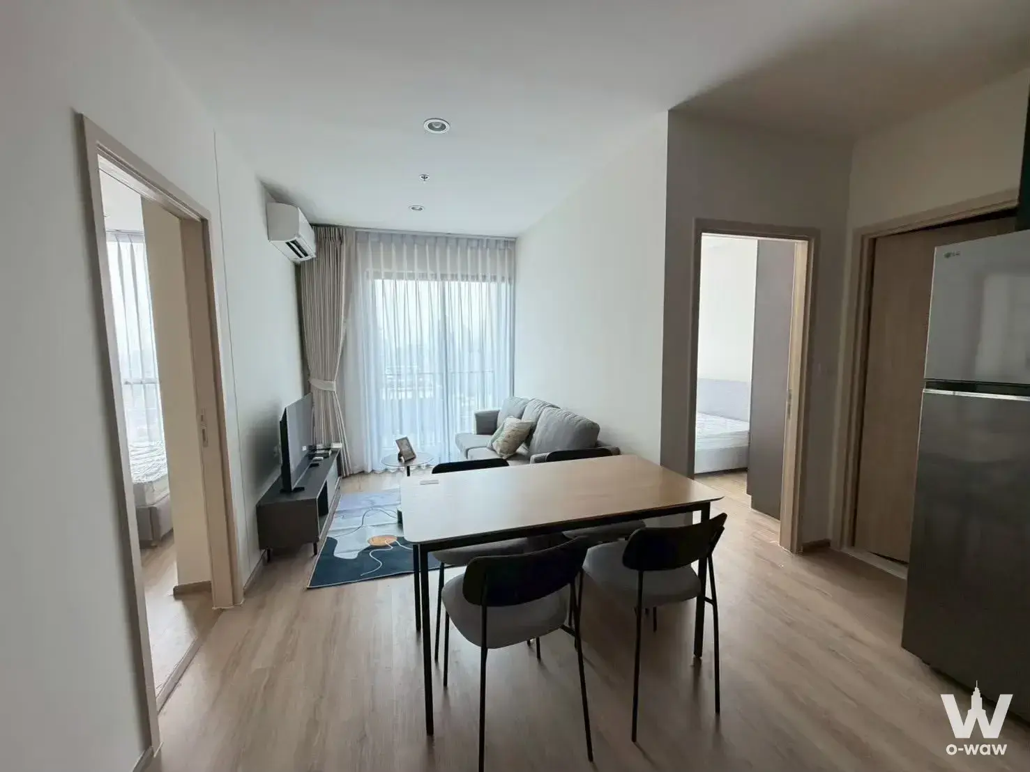 Open-plan living space in a Nue District R9 rental with grey sofa, dining table, and bright natural light