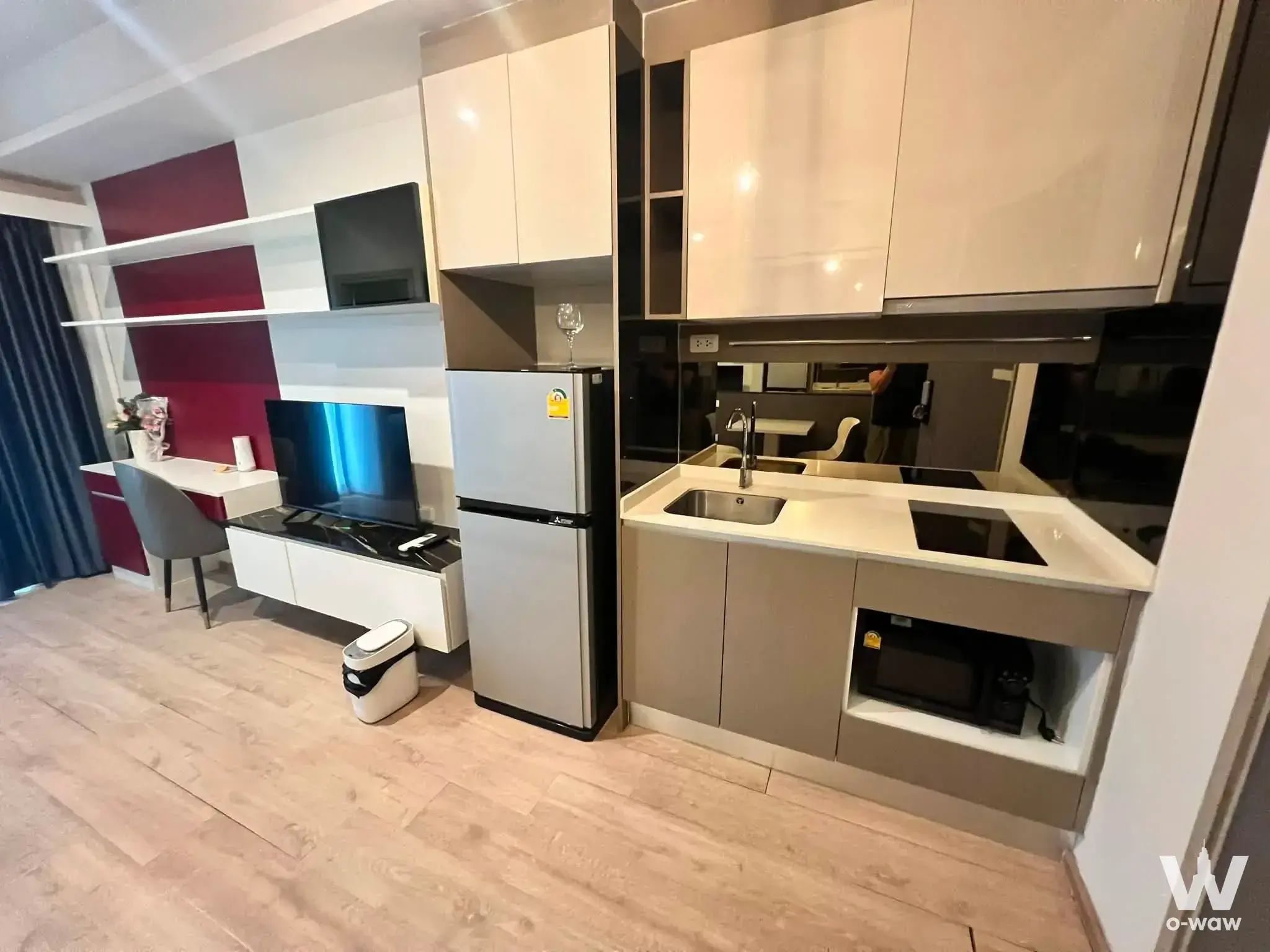 Open-plan 1-bed condo in IDEO Rama 9 with red accent wall, dark blue curtains, and compact kitchen