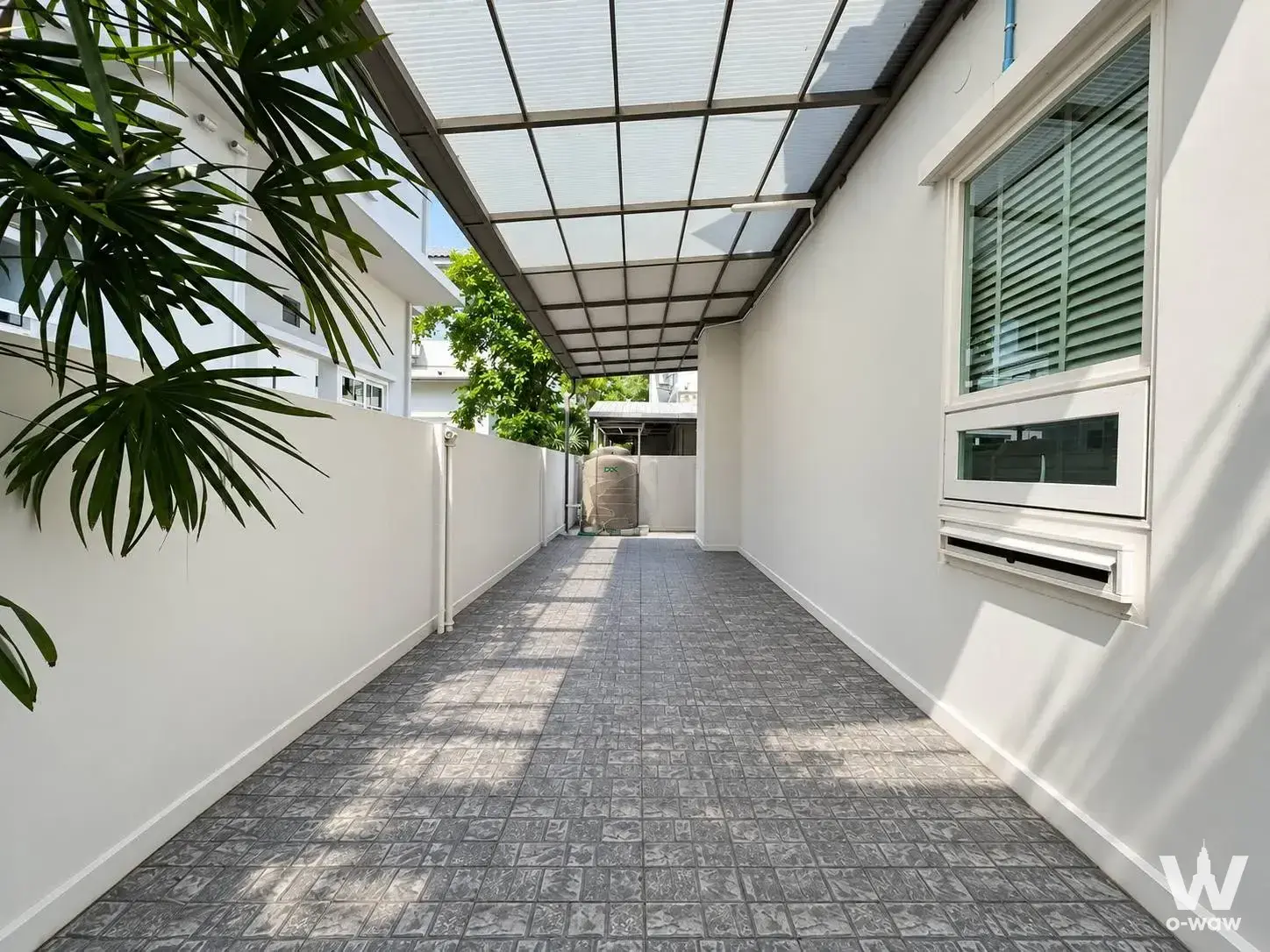 3-bed house for sale in Manthana Bangna-Wongwean showing an outdoor covered walkway with dappled sunlight and green accents