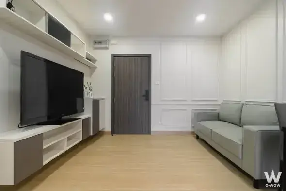 Living room with wall-mounted TV, floating shelves, and grey sofa in Supalai Veranda Phasi Charoen Station