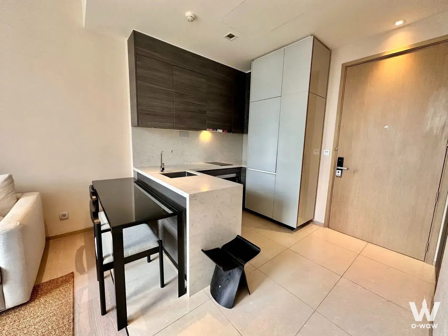 Open-plan kitchenette in a 1-bed condo for rent at THE ESSE ASOKE with dark wood cabinets, quartz island, and black glass