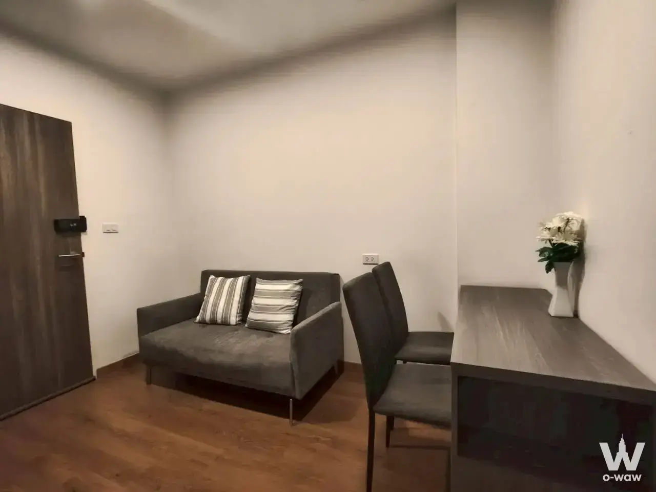 Magnix Condo Ramintra21 1-bed studio living area with grey sofa, striped pillows, and dark wood flooring