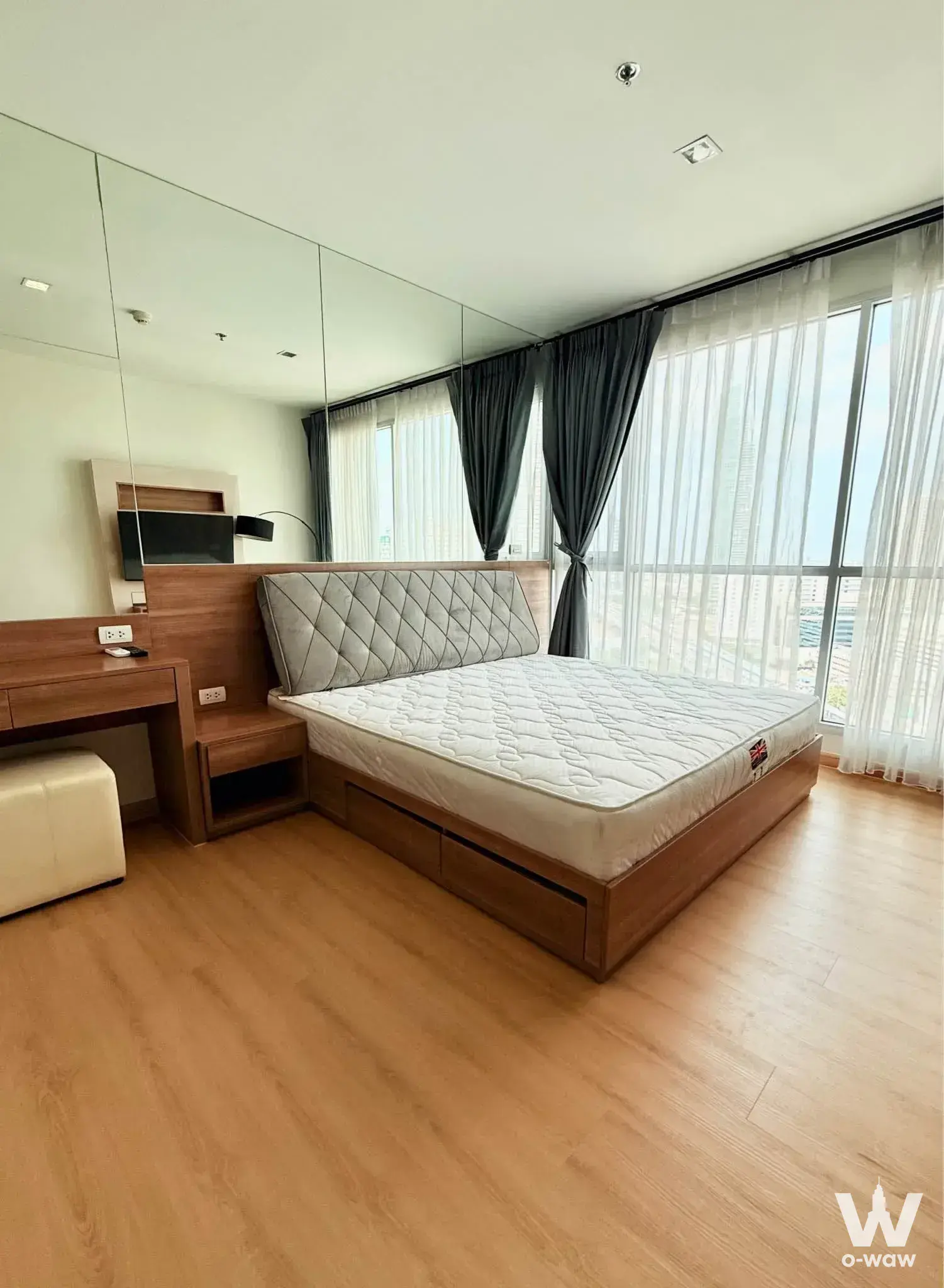 Bedroom in a 2-bed RHYTHM Sathorn condo rental with mirrored wall, storage bed and floor-to-ceiling city windows