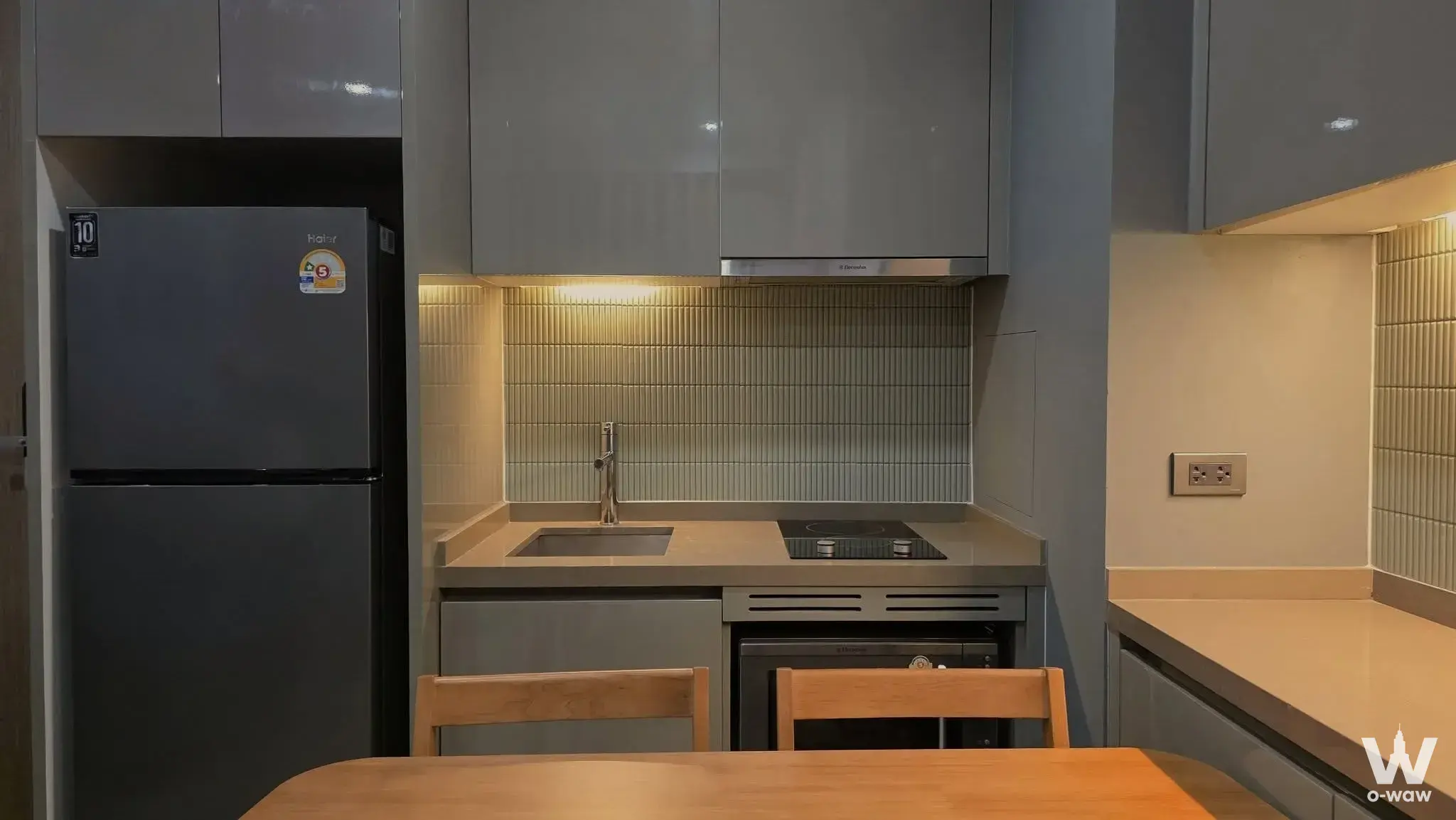 M Silom 1-bed condo kitchen has grey cabinets and a black glass cooktop