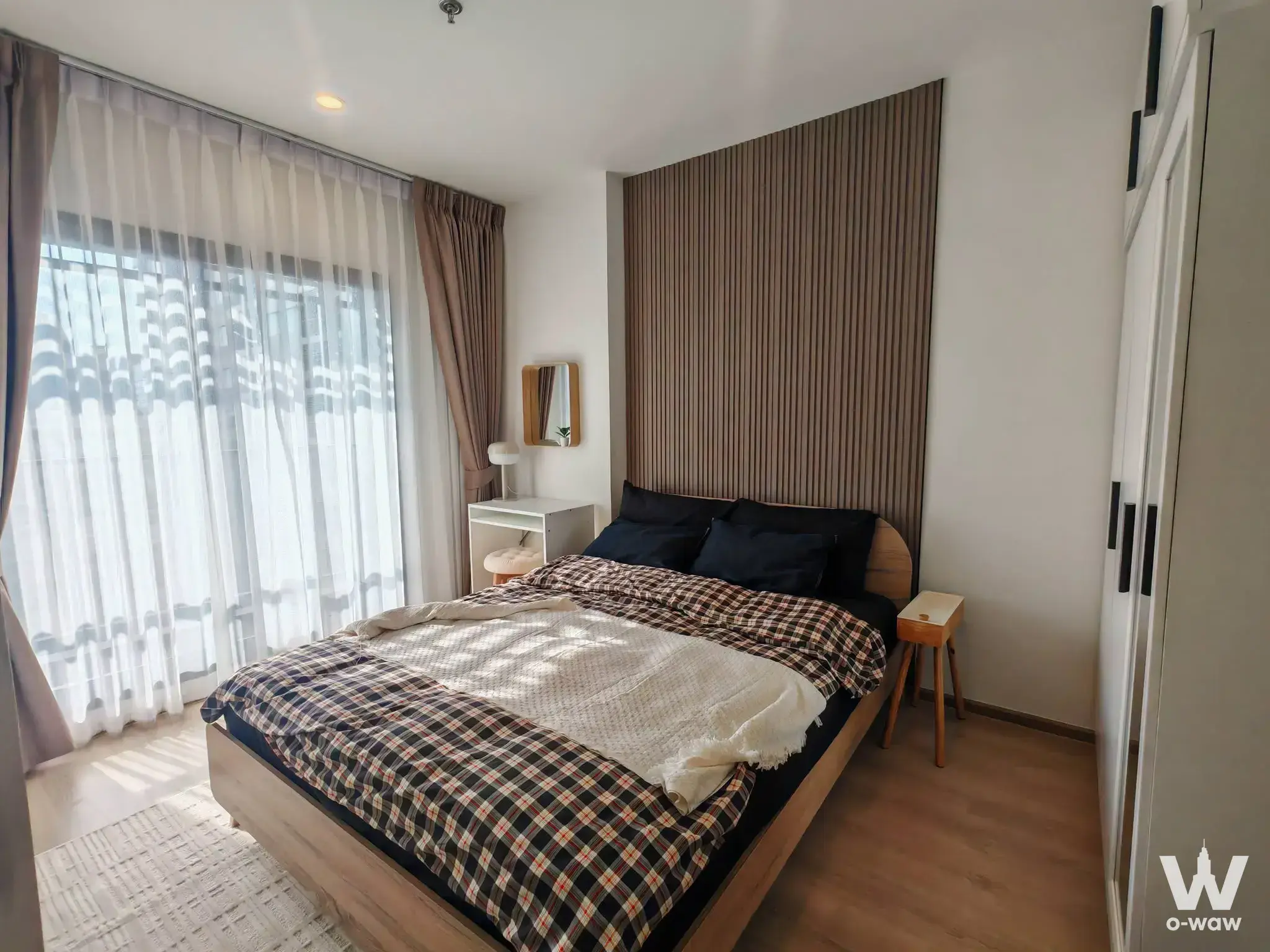 The bedroom of this 1-bed condo in Life Rama 4 - Asoke has a queen bed, plaid comforter and full-height window