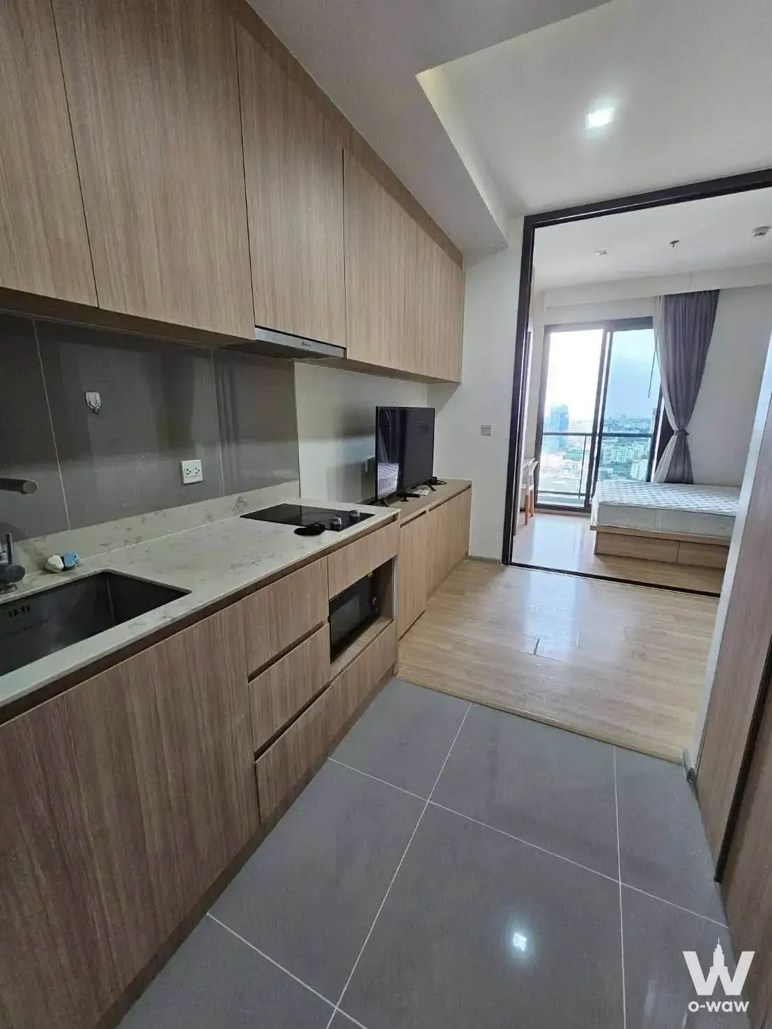 Modern M Jatujak 1-bed kitchen with light wood cabinetry, marble countertop, and bedroom view