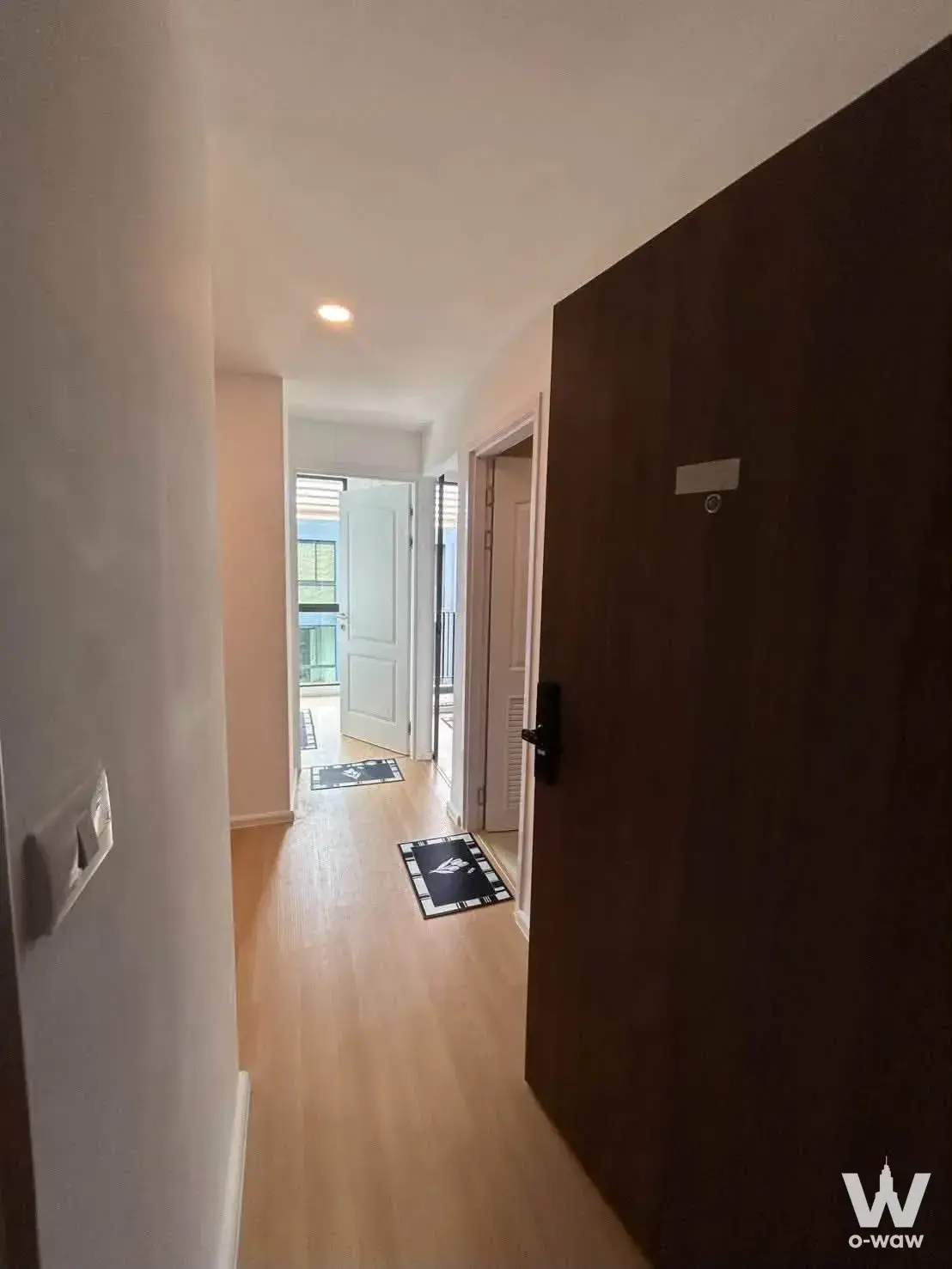 Entry hallway of a 1-bed condo for sale in Cerocco Bangna 36 with light wood laminate floors and a dark brown entrance door