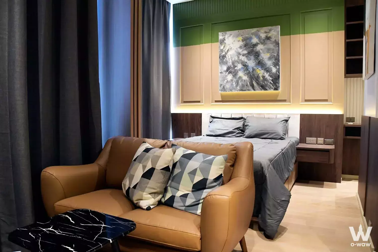 Luxury bedroom in Ashton Silom featuring forest green walls, tan leather loveseat, and herringbone oak flooring