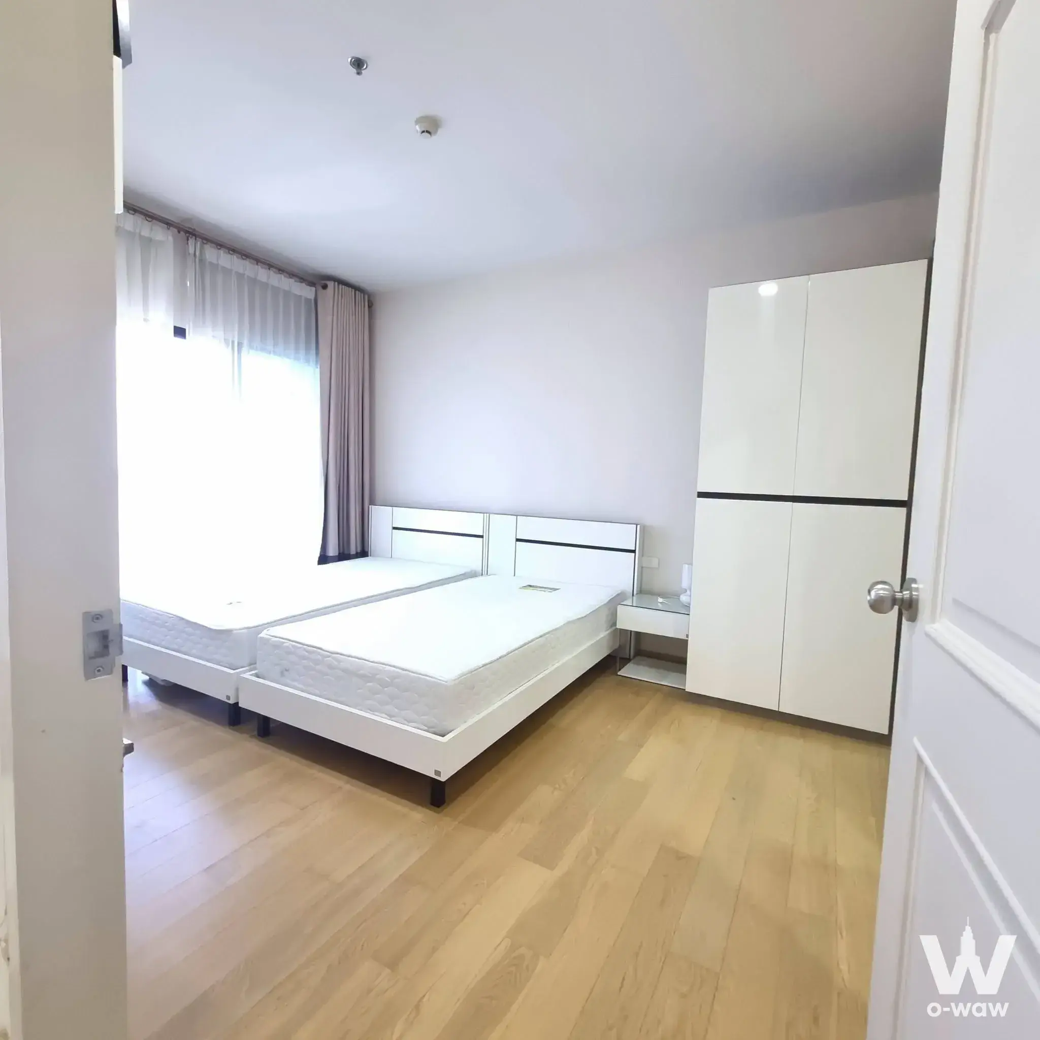 1-bed condo for rent in Noble Reform featuring a minimalist bedroom with two single beds and a glossy white wardrobe