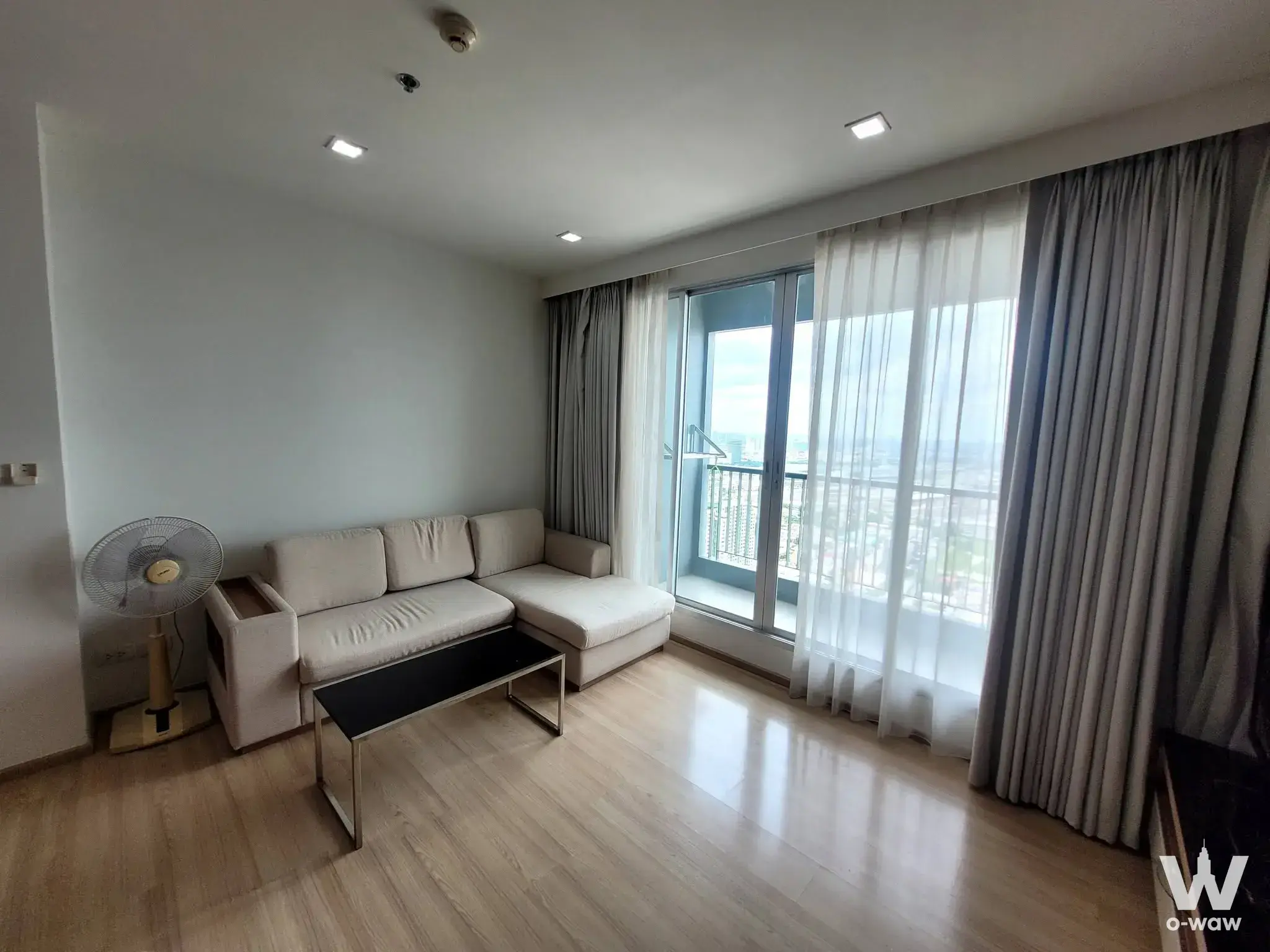 Modern living room in RHYTHM Phahon-Ari featuring a beige sectional sofa and city skyline view
