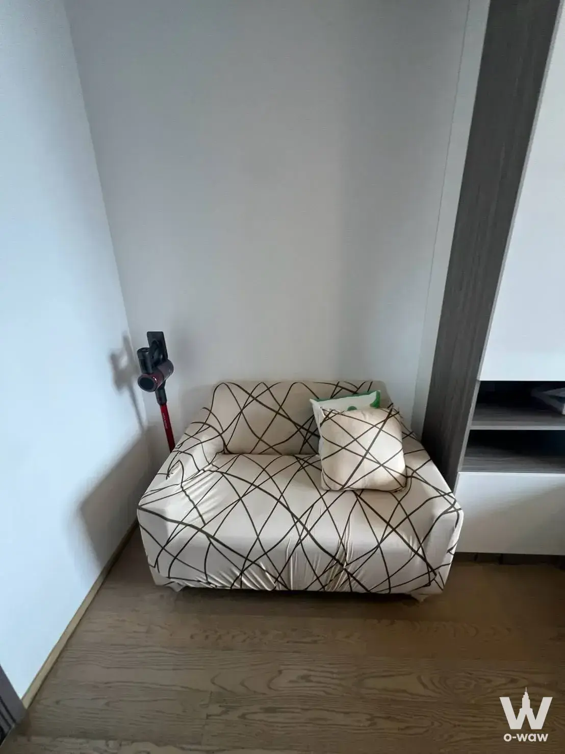 Compact studio corner at Ashton Chula-Silom with patterned armchair, built-in cabinetry and wall-mounted vacuum