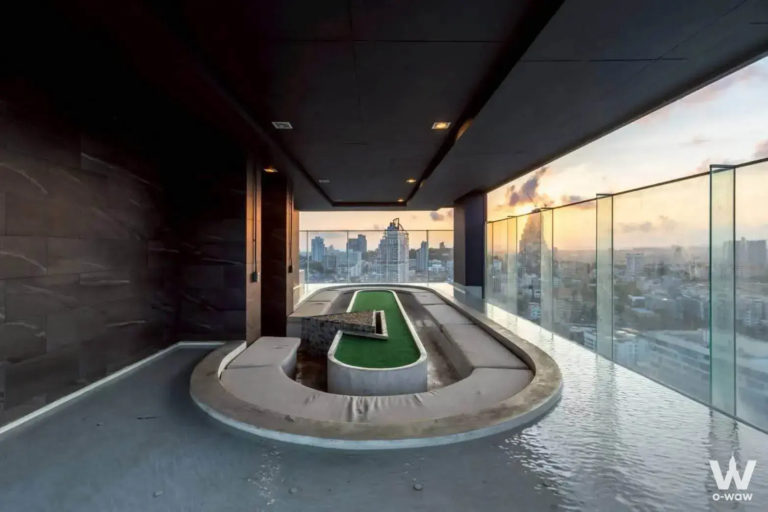 Infinity pool deck at The Panora Pattaya condo featuring an oval turf island and city skyline views