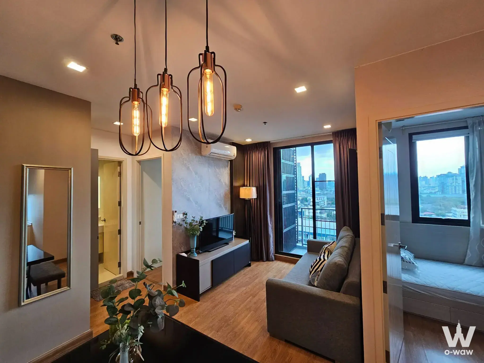 Modern living room in a 2-bed Q House Sukhumvit 79 condo with grey sofa, industrial pendants, and city view