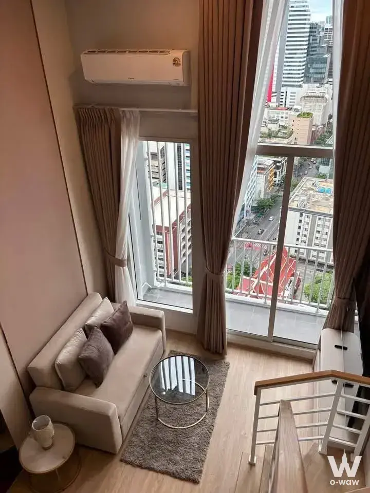 0-bed loft living room in Culture Chula with beige sofa, glass coffee table, and city street view through windows