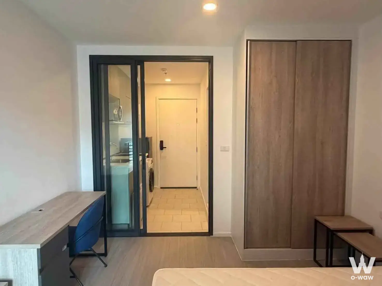 Bedroom in a DENIM Jatujak condo with a light wood desk, built-in wardrobe, and open view to the kitchenette