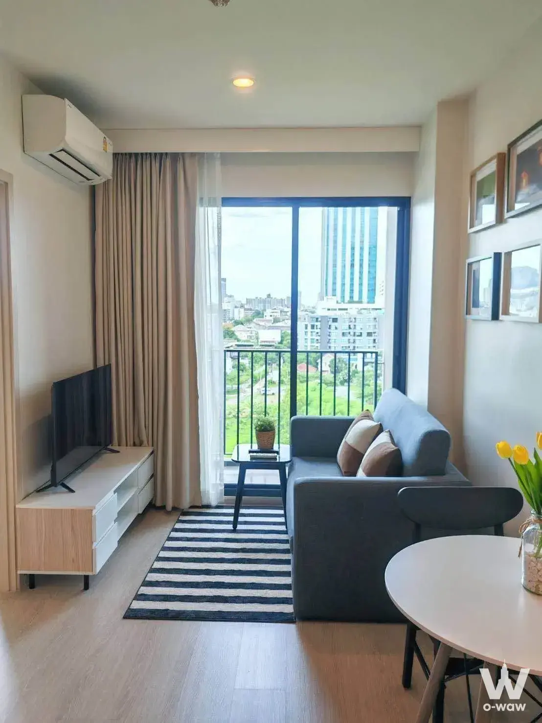 The living room in a 1-bed condo for sale in NUE Noble Ratchada Lat Phrao has a grey sofa, TV console and balcony city view
