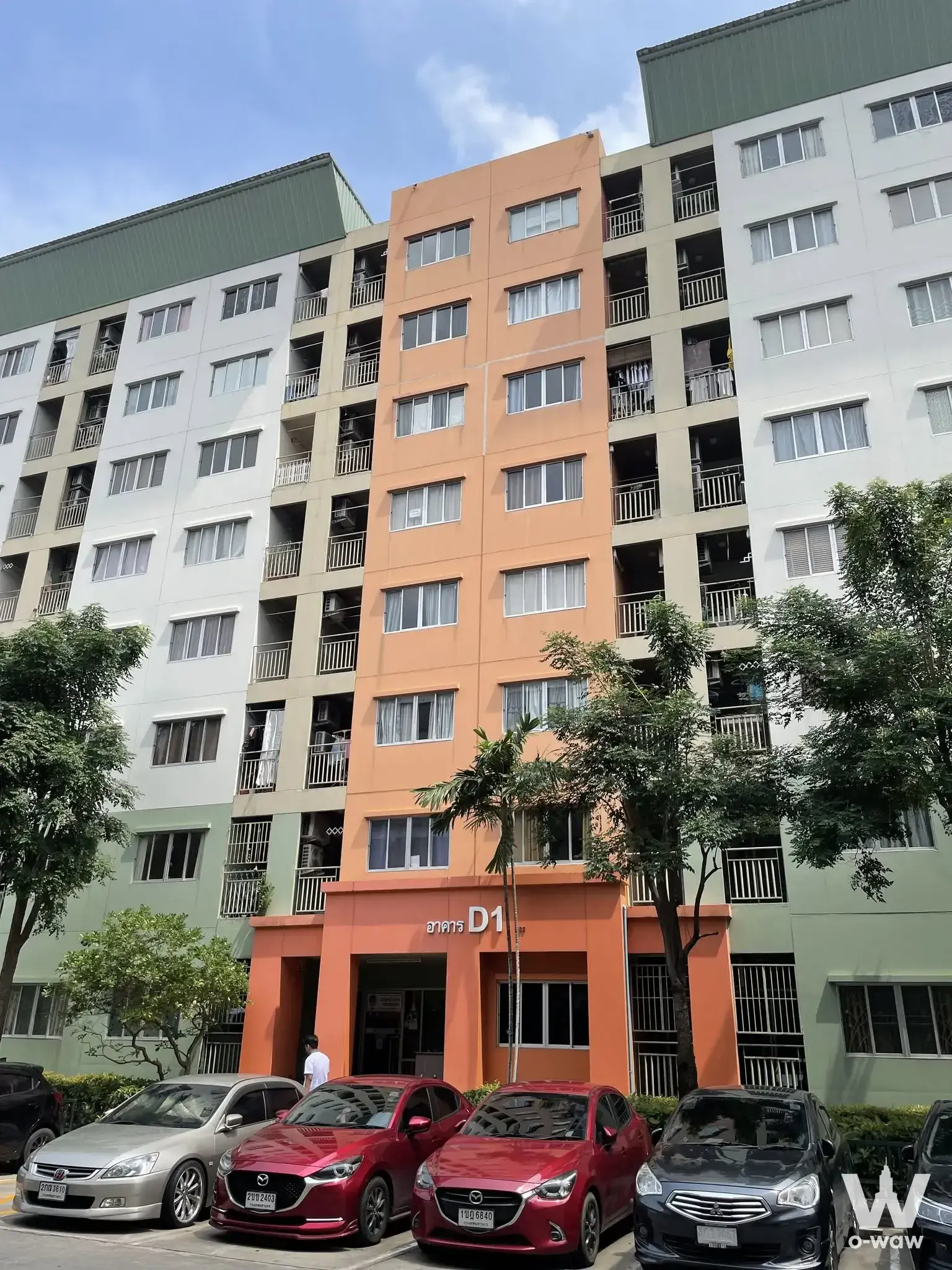 Bright orange and white exterior of Lumpini Condo Town Bodindecha-Ramkhamhaeng with balconies and parking lot