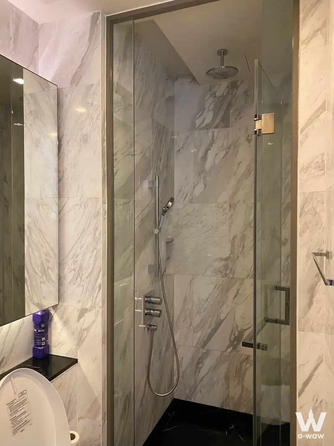 Saladaeng One bathroom with white veined marble tiles and glass shower enclosure